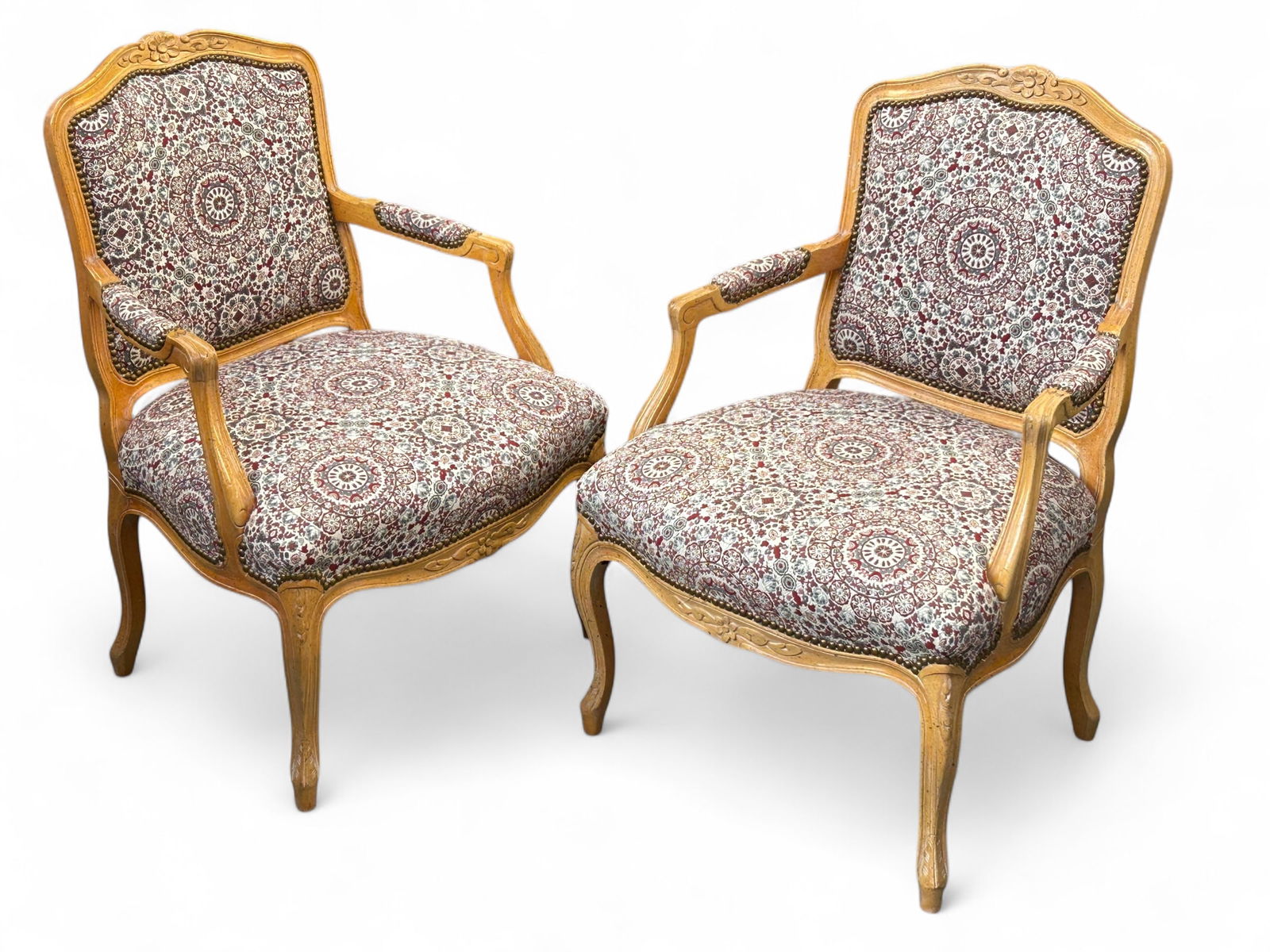 Pair of French Carved Armchairs.: Both of these bergere chairs have floral upholstered seats and backs, light wood frames, carved details, and brass nailhead trim. There are minor scratches, but overall, they are in good condition. Ea