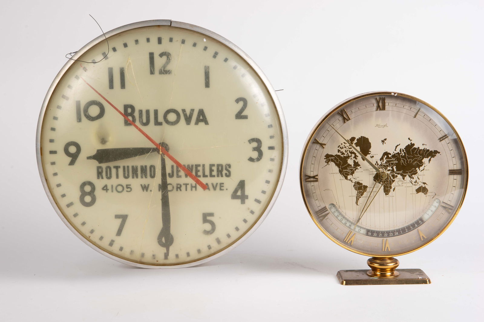 Lot: Kienzle World Time Clock & Advertising Clock.: Neither clock seems to be ticking, although the advertising clock has at least one light socket which lights it up. The vintage advertising clock is a Bulova dealer's clock for Rotunno jewelers in Chi