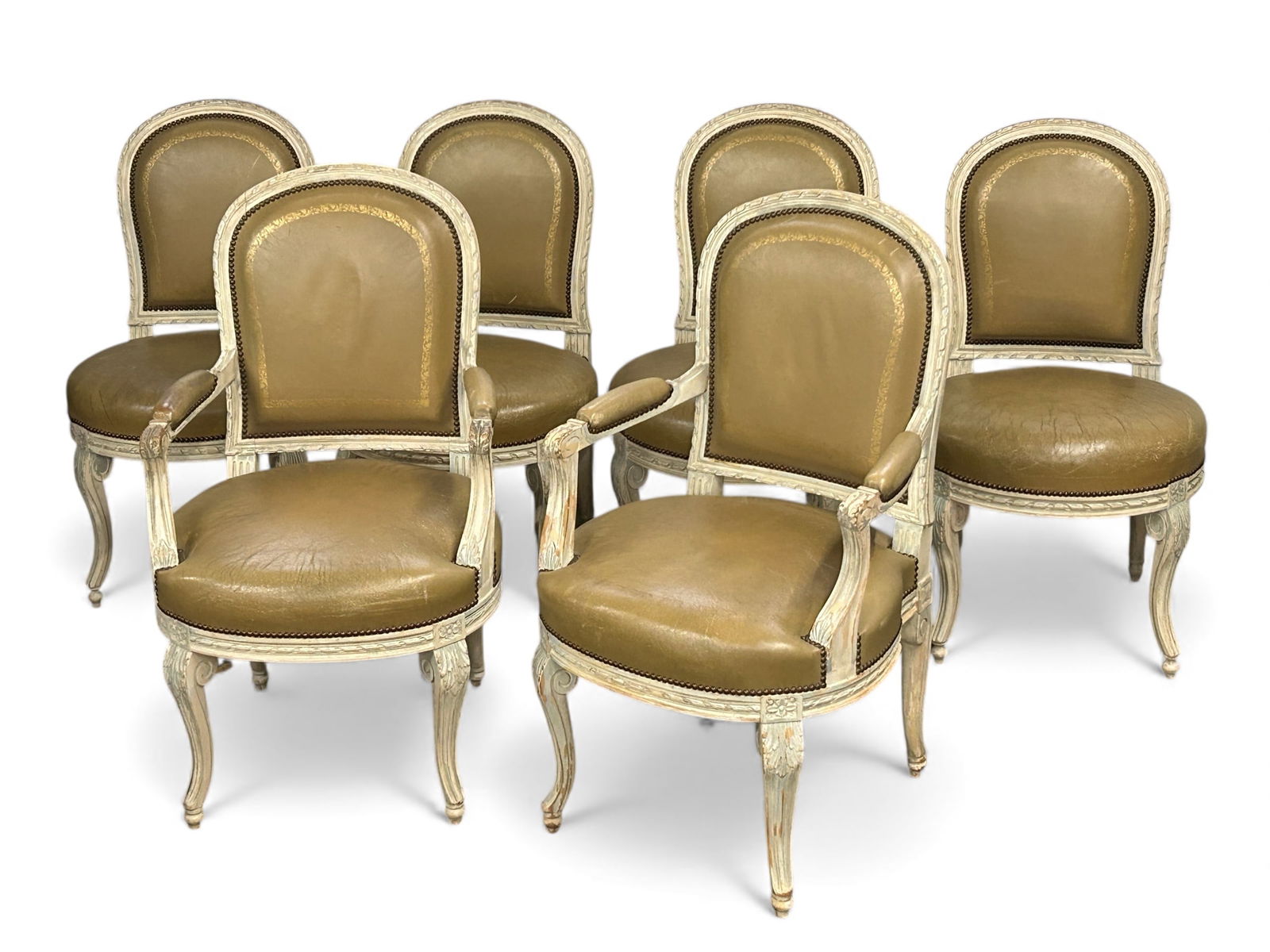 Set of Six French Dining Chairs.: These chairs (two of which have arms) have brown leather seats and backs, carved wood frames, brass nailhead trim, and floral details. There are some scratches, and the leather seats have wear marks a
