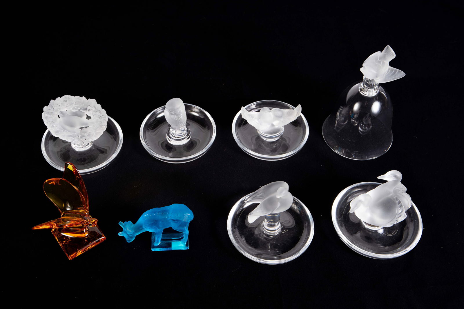 Lot of Mostly Lalique Ring Dishes, Bells, Animals.: This lot includes five Lalique bird-themed ring dishes, a Lalique bell with bird, and a blue Lalique deer figural paperweight. Also included is an amber colored Baccarat butterfly. Overall, the lot lo