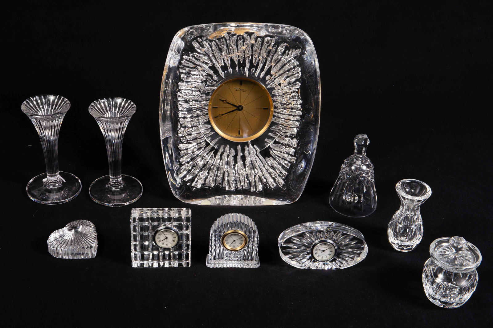 Lot of Mostly Waterford Crystal Table Articles.: The lot includes desk clocks, a heart paperweight, a bell, a pair of candlesticks, a condiment jar with lid, a small vase, and a Daum France "Anemone" easel back clock. This is the largest item in the