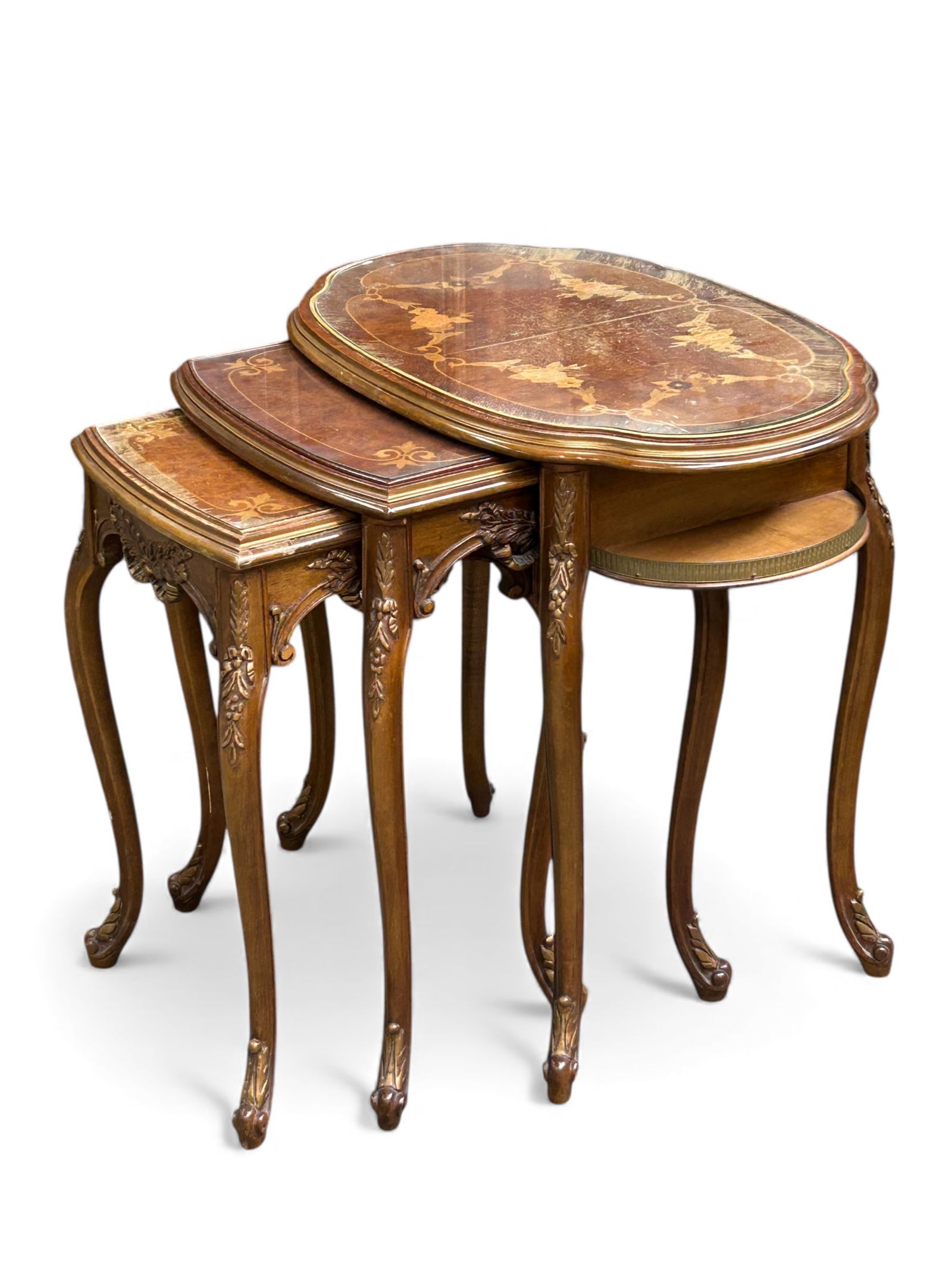 Set of Three French Carved Nesting Tables.: These Louis XV tables feature satinwood inlaid marquetry, protective glass tops, carved aprons, and carved legs. The largest table has a brass gallery. There are water stains and marquetry loss, as we