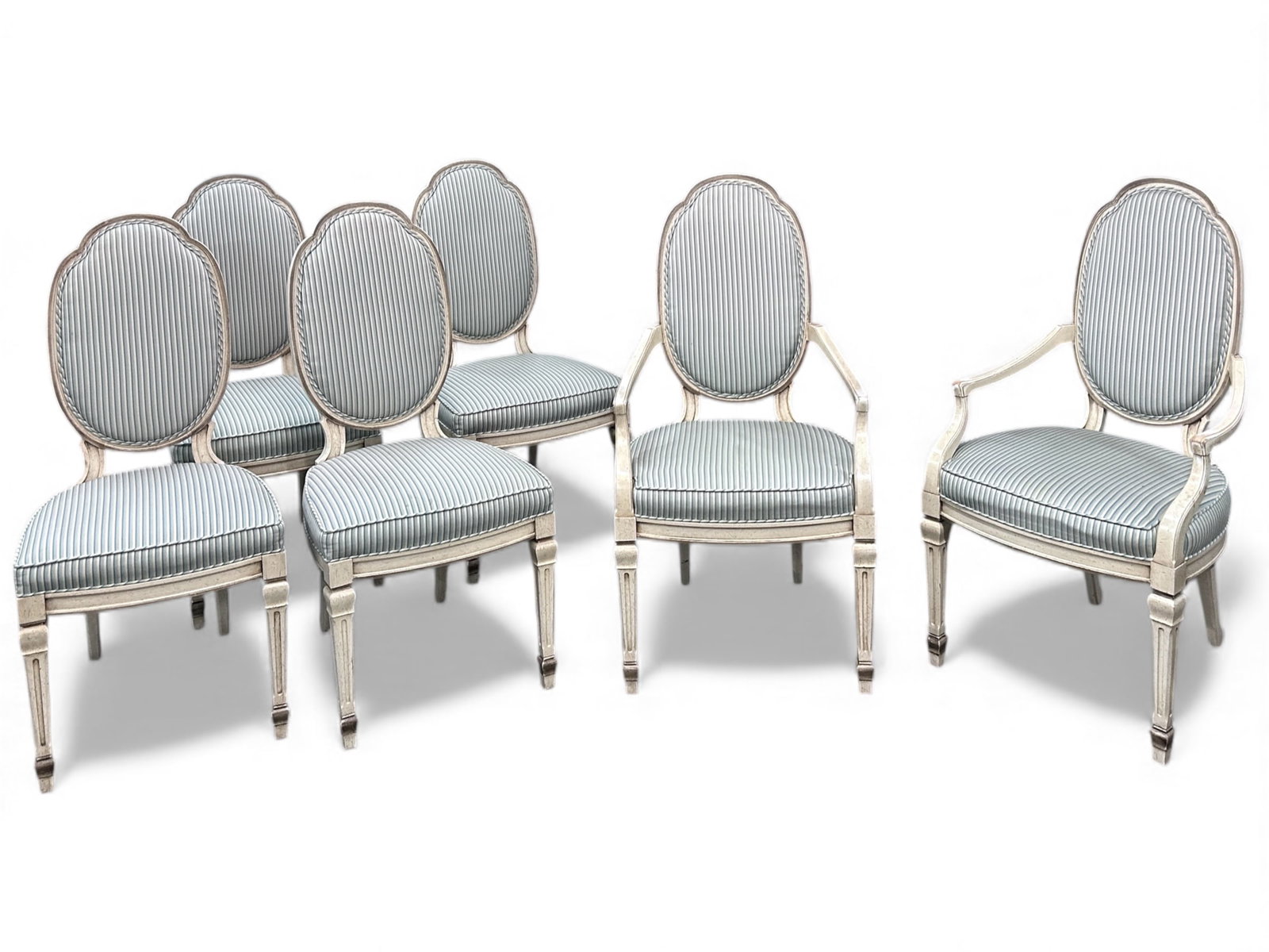 Set of Six French Carved Dining Chairs.: These chairs have oval shaped backs, cream colored frames, and striped upholstery. Two have arms. There are some scratches on the frames and dirt spots on the seats. One of the chairs has a crack on t