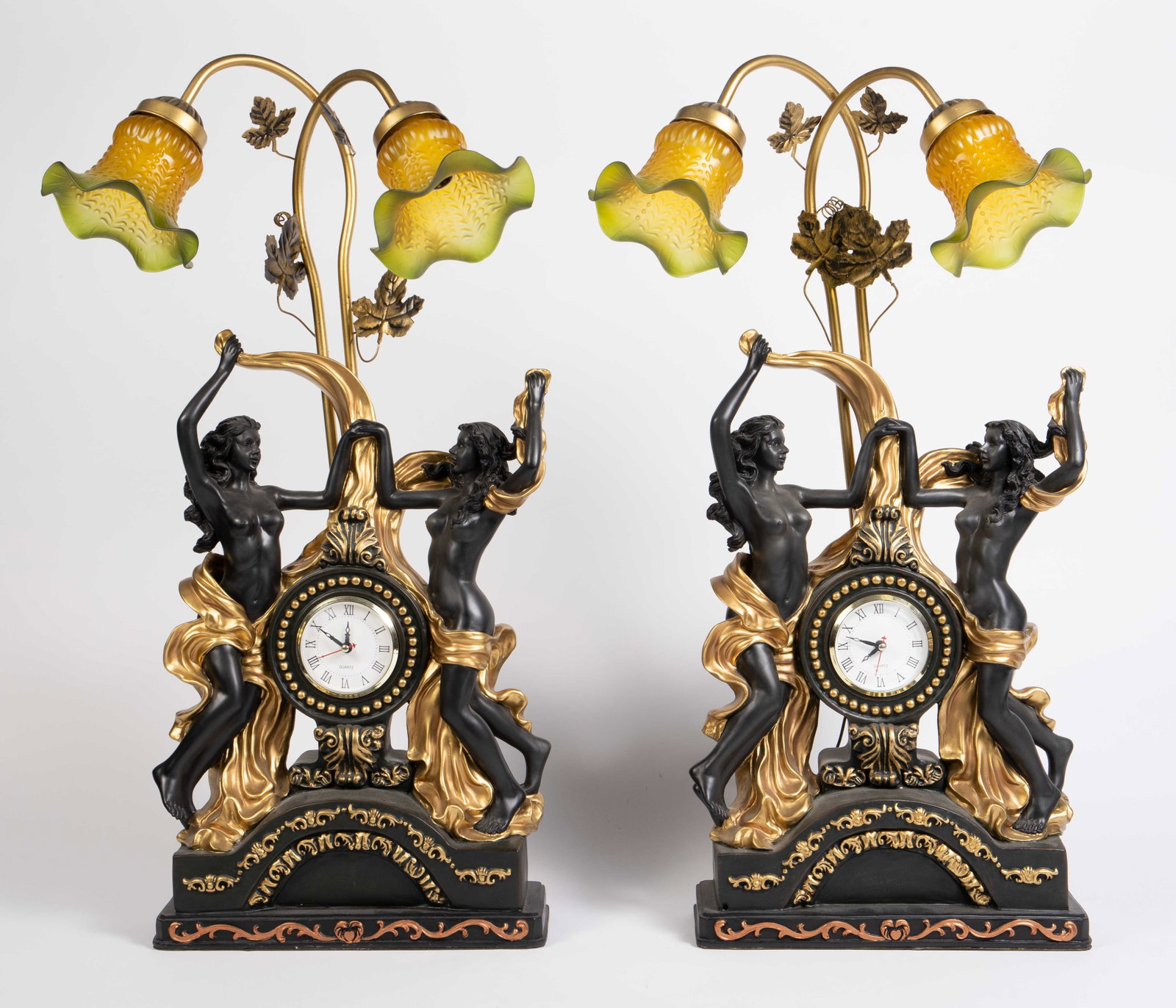 Pair of Nude Female Lamps w/ Iridescent Shades.: Each black and gold clock has a central dial that is flanked by nude ladies, and two vine-like necks that support flower-shaped shades. Overall, they look to be in good cosmetic condition. The materia