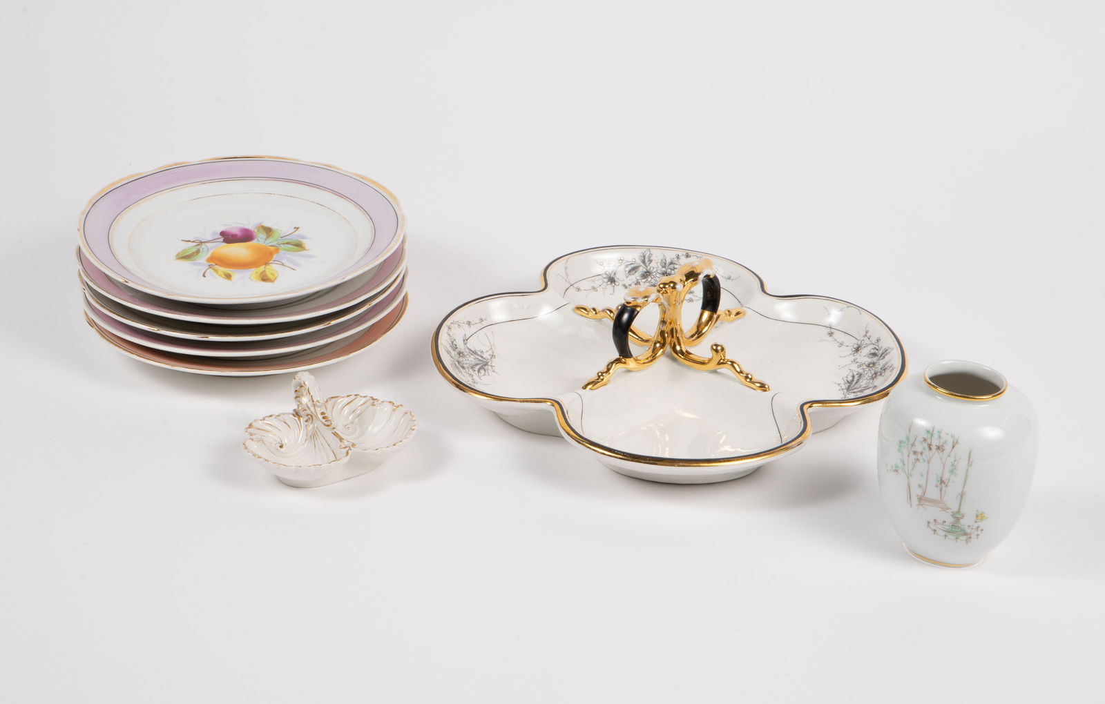 Lot of Assorted KPM Germany Porcelain.: This lot includes the following: a set of 5 plates with fruit designs, a small vase with an image of a park fountain, a shell-like condiment dish or salt and pepper dish, and a gold-handle snack tray.