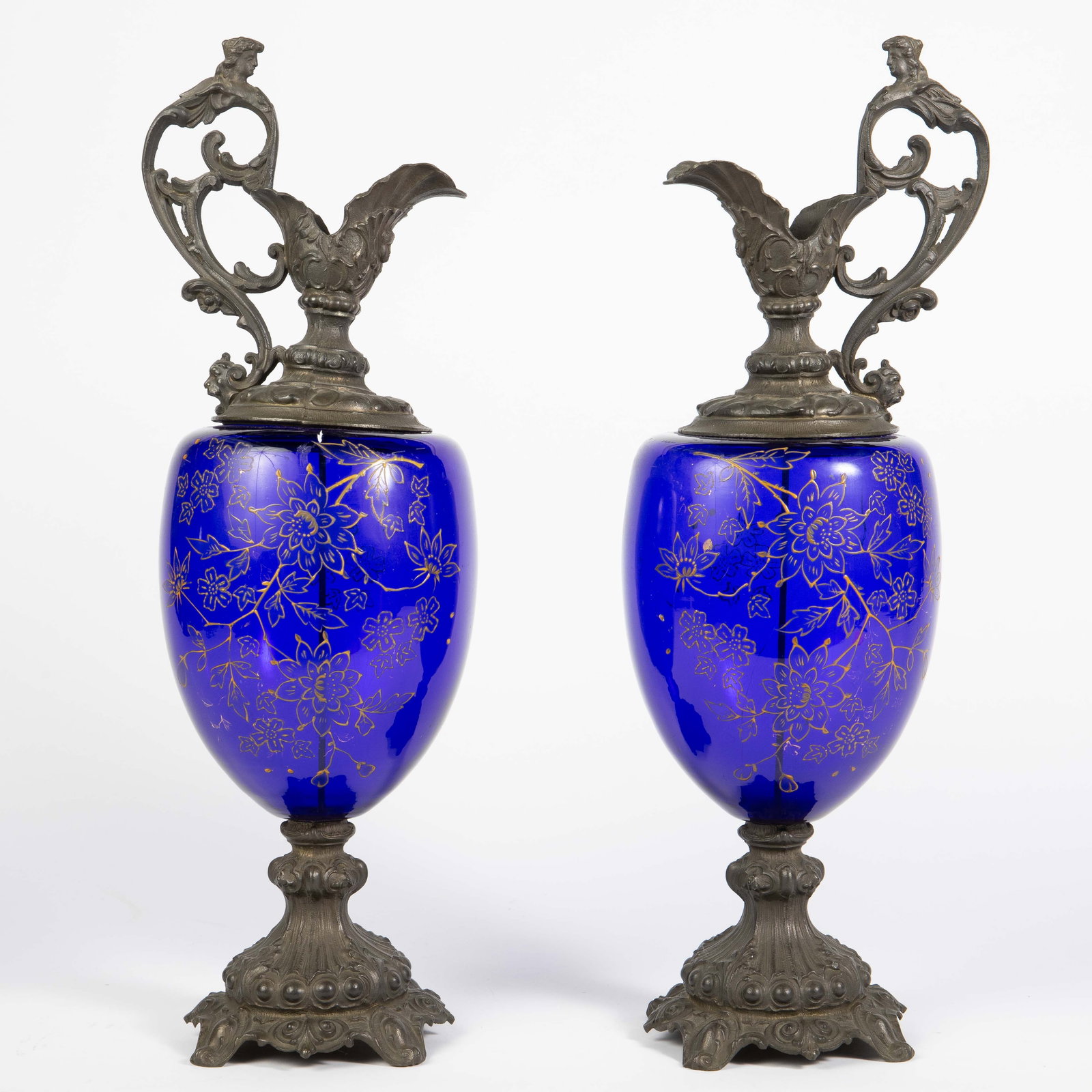 Pair of Victorian Ewer-Shaped Cobalt Garnitures.: The pair of ewer shaped cobalt glass and cast metal garniture have a patinated bronze finish, and hand painted enamel flower decorations on the glass. The tops of the pieces feature face decorations,