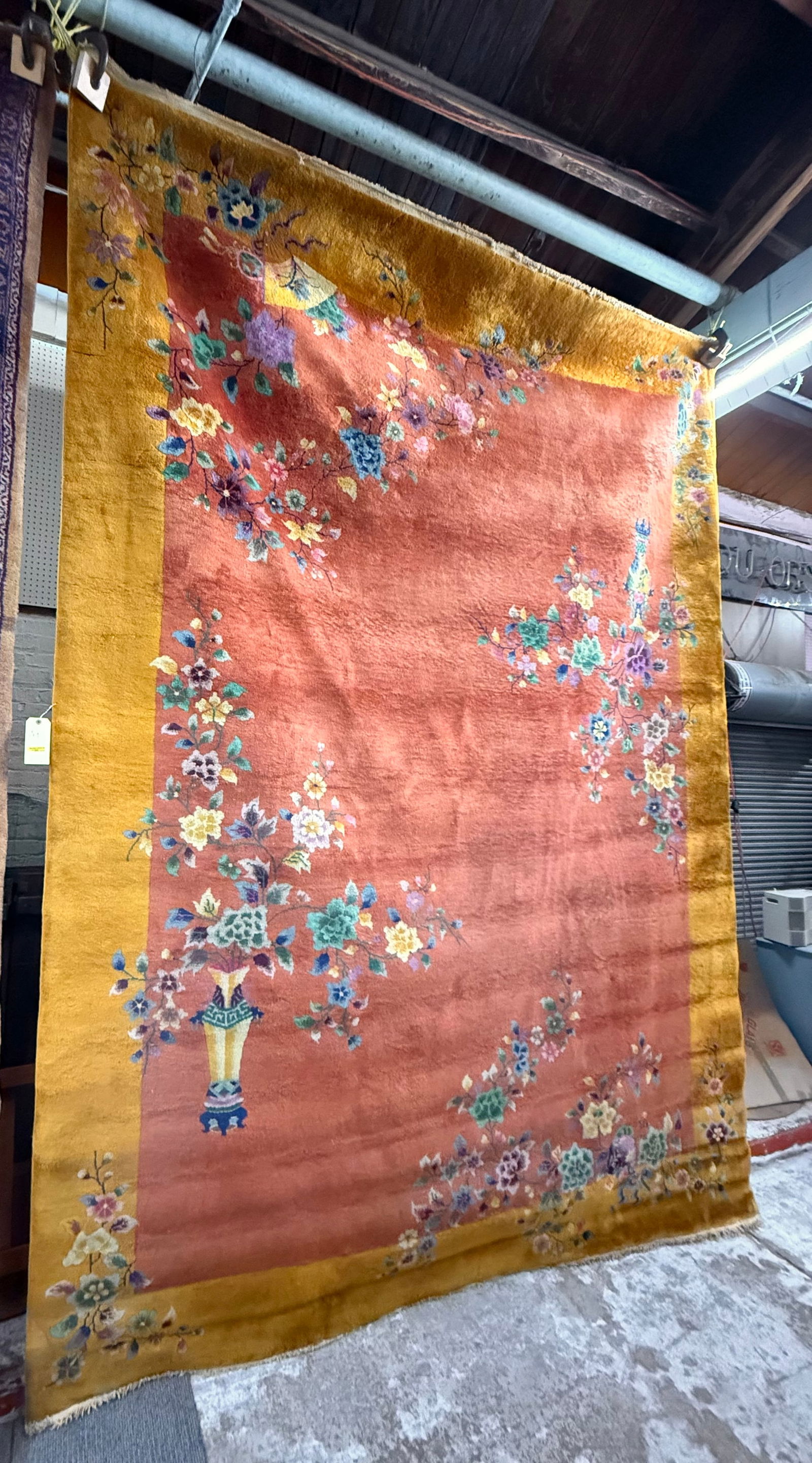 11' 9" x 9' Chinese Art Deco Rug.: This rug has a rust or salmon color field with a gold border. It is adorned with designs of flowers, vases, and a fan. It looks to be in good overall condition for its age. In-house shipping is availa