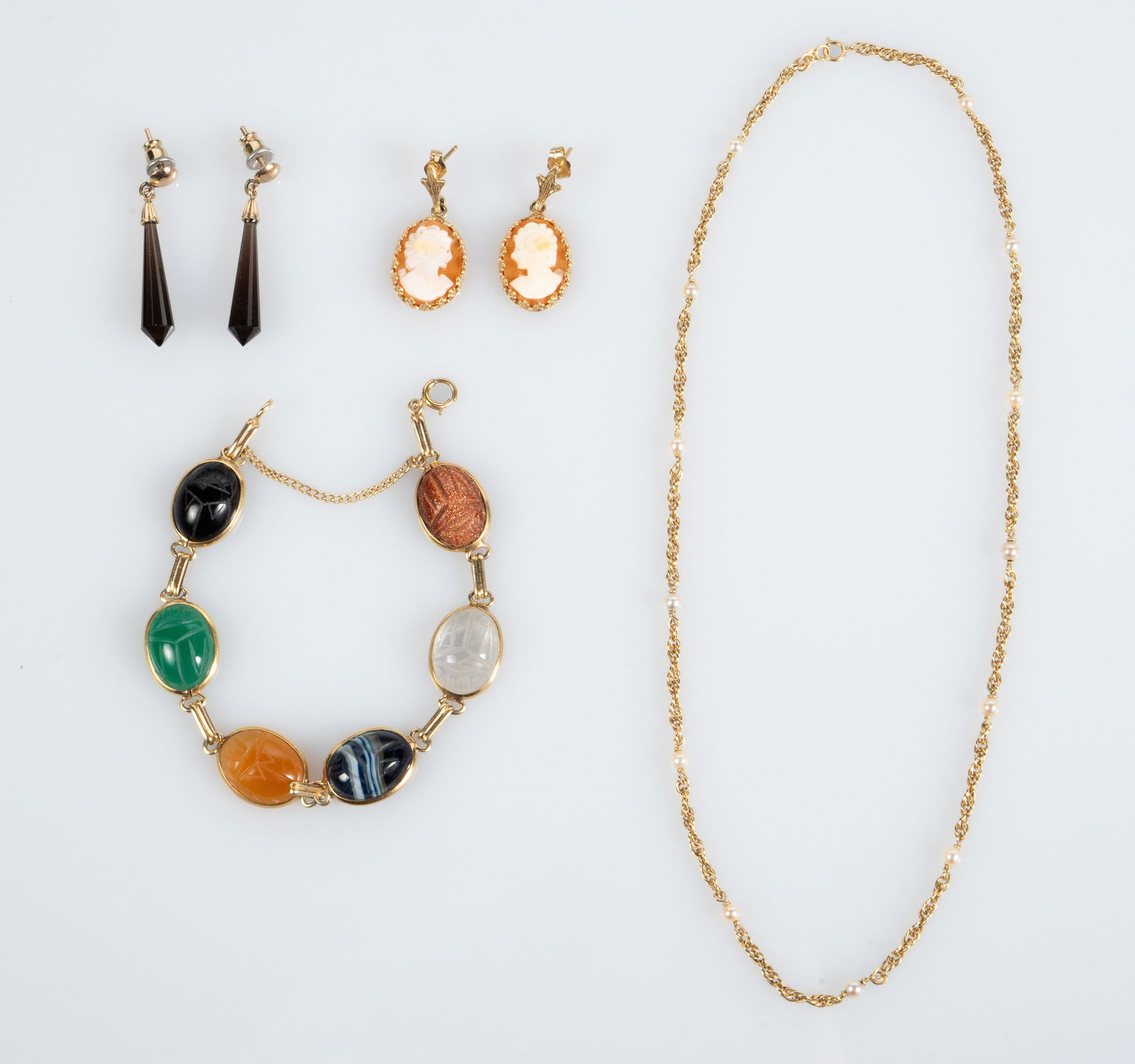 Lot of 14K Gold Jewelry - Cameo, Scarab, Pearls.: The lot contains 4 pieces of 14K gold jewelry. There is a pair of earrings with onyx prisms, a pair of carved coral cameo earrings, a necklace with several small pearls, and a bracelet with carved sca