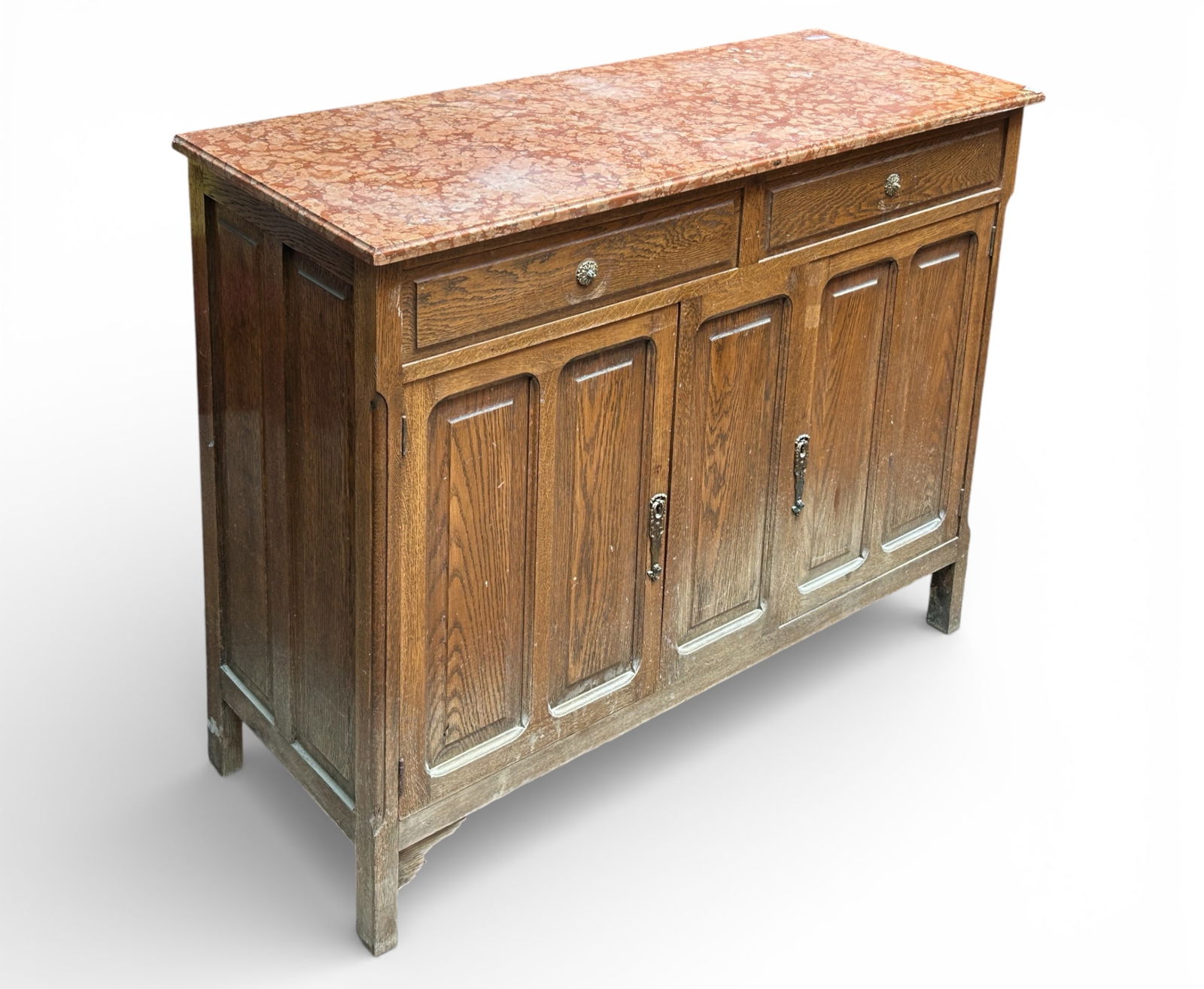 Marble Top Oak Sideboard.: The sideboard has a bevelled pink speckled marble top, two upper drawers, two lower doors, panelled sides, fixed interior shelves, and brass decorated hardware. The hardware on the top is missing the