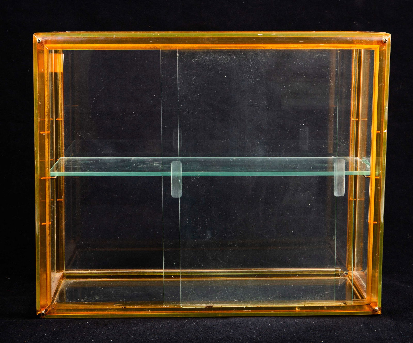 Tabletop Display Cabinet w/ Apple Juice Bakelite.: The small unusual glass display cabinet has a yellow tone or apple juice bakelite frame, with rounded edges and corners. The cabinet has one glass shelf and two sliding doors on one side, with recesse