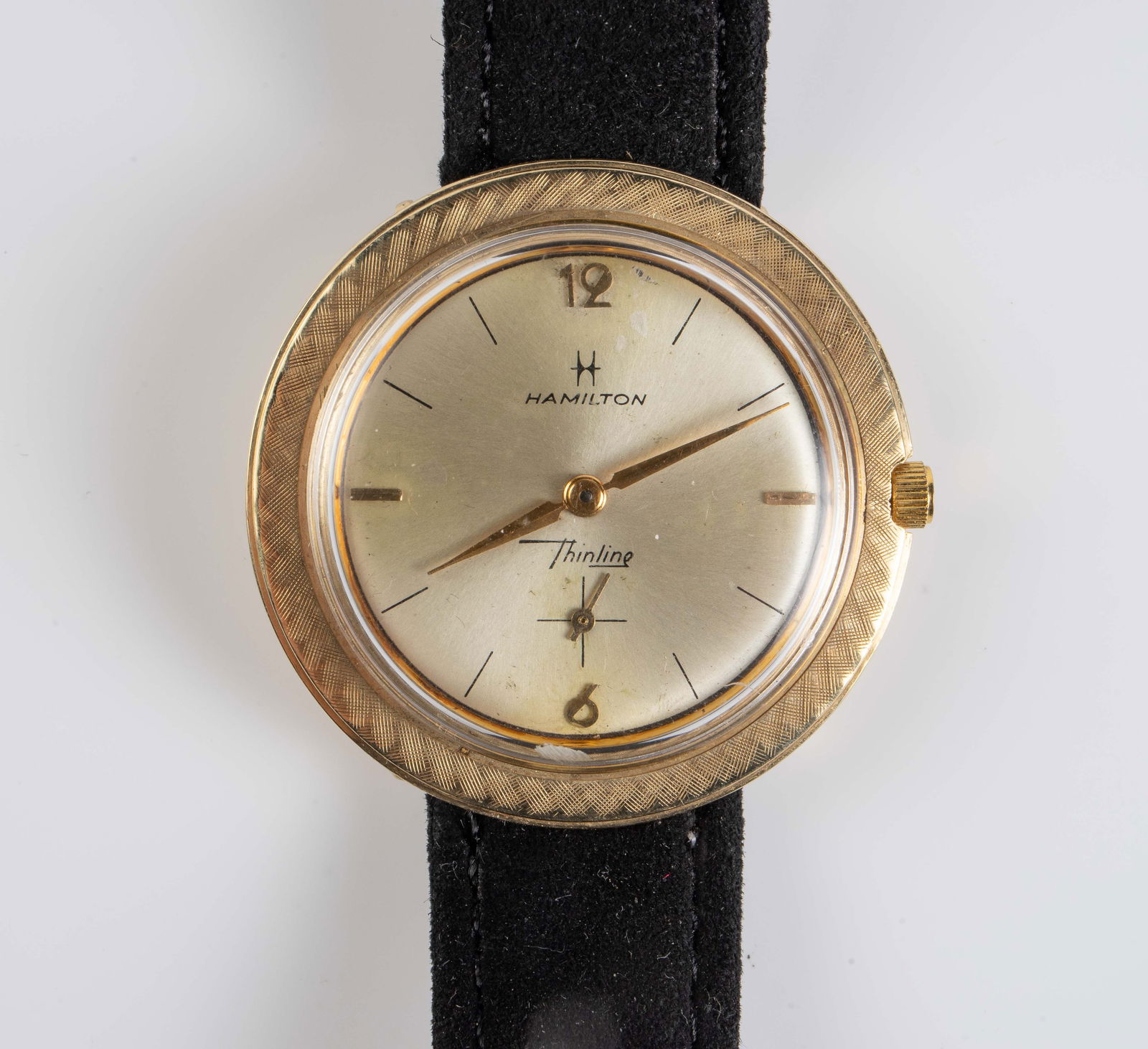 Hamilton Thinline 14K Yellow Gold Watch.: The watch features an etched bezel. It is unmarked, but tested appropriately for 14K gold. It has a black suede band. The case measures 35mm in diameter. It is not currently ticking. The piece weighs