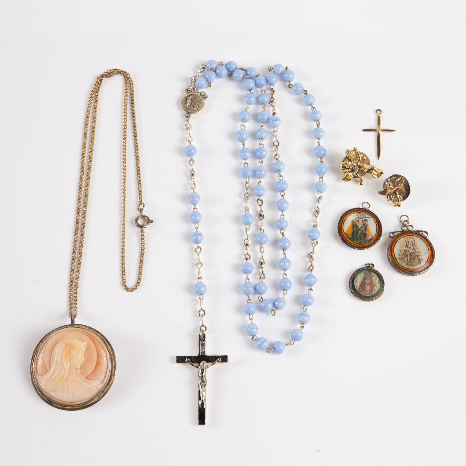 Lot Virgin Mary Cameo, 14K Cross, Painted Pendants: The religious lot contains 8 items. There is a carved coral Virgin Mary cameo pendant in an 800 silver setting, an Italian rosary with blue (likely) glass beads, 2 cherub pins, and 3 handpainted saint