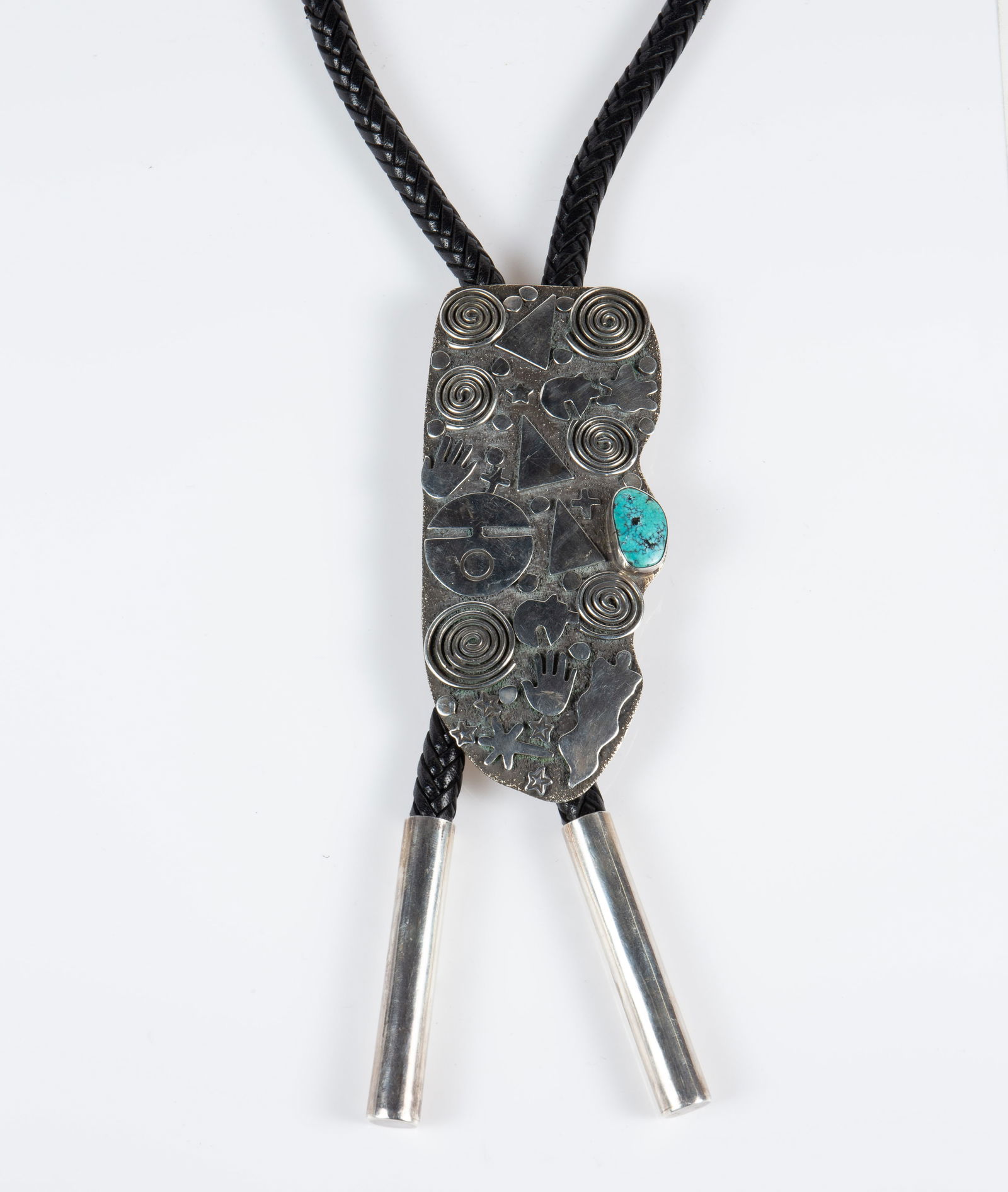 Alex Sanchez Sterling Silver Petroglyph Bolo Tie.: The Native American Indian bolo tie is marked Alex Sanchez Sterling on the back. It features the artist's emblematic "Petroglyph" designs, and a single turquoise stone. The slide measures 4 3/4" x 2 1