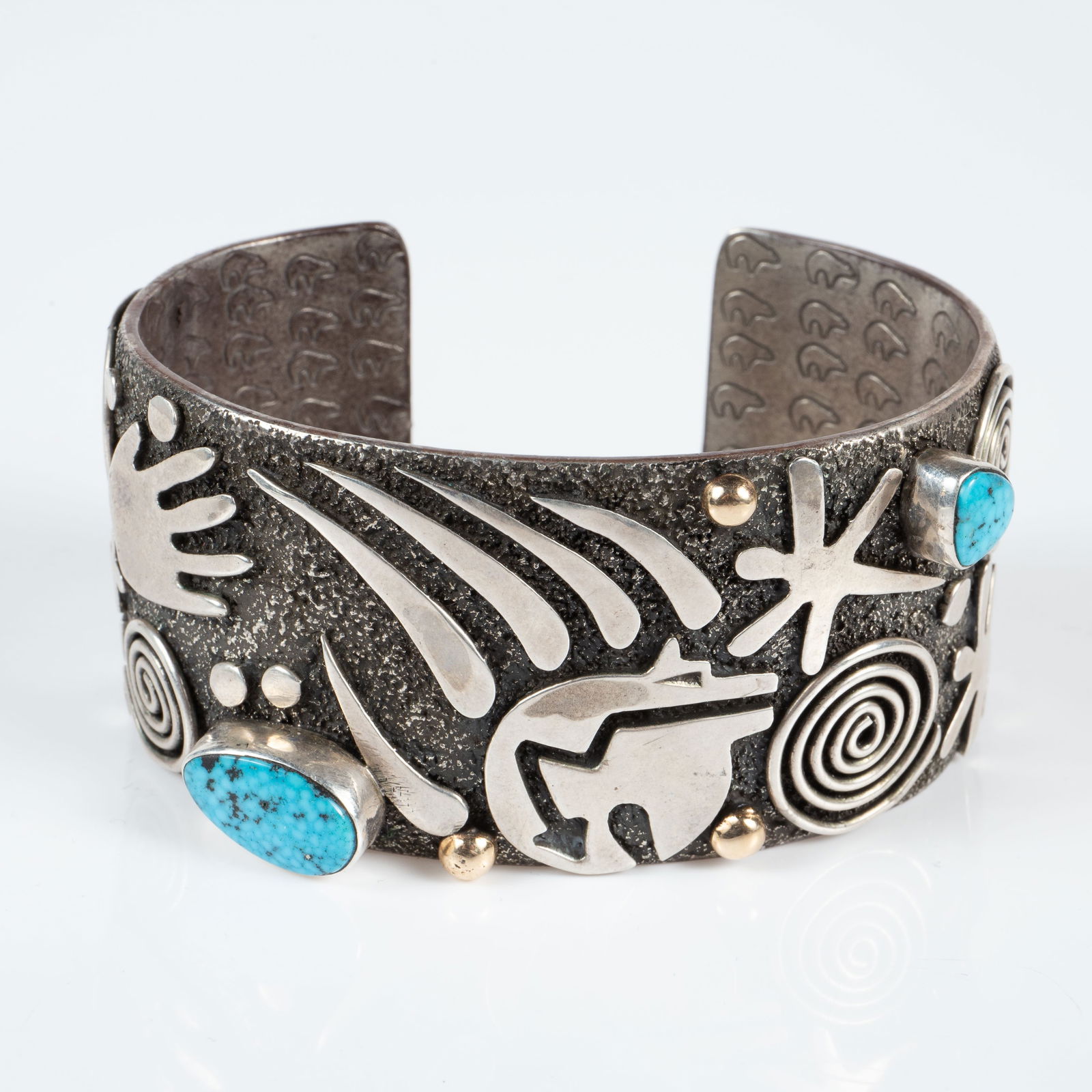 Alex Sanchez Sterling 14K Petroglyph Cuff Bracelet: The Native American Indian bracelet is marked Alex Sanchez Sterling on the back. It features the artist's emblematic "Petroglyph" designs, a couple of sleeping beauty turquoise stones, and three 14K g