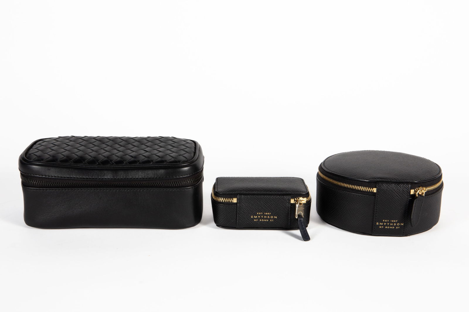 Bottega Veneta & Symthson Black Leather Cases.: The lot contains 3 designer black leather zippered cases. First, there is a Bottega Veneta interecciato pouch with brown suede lining. It measures 4" tall, 7 3/4" wide, and 3 3/4" deep. It still has