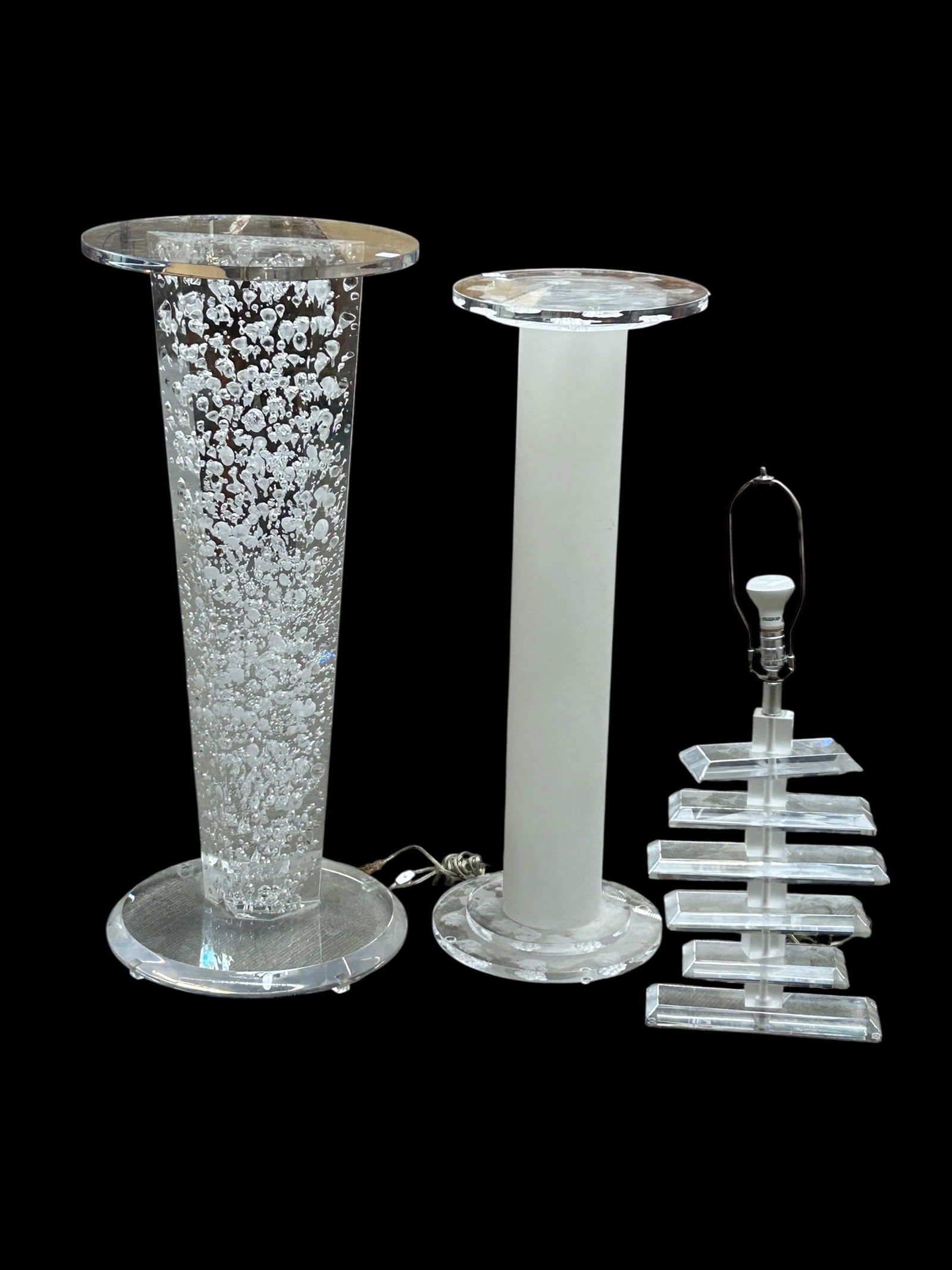 Two Lucite Pedestals & One Lamp.: This lot consists of a frosted glass acrylic tubular pedestal with a round clear lucite top, and a base that has a floral textured design. It measures 39 1/2" tall, with a 14" diameter. The tall