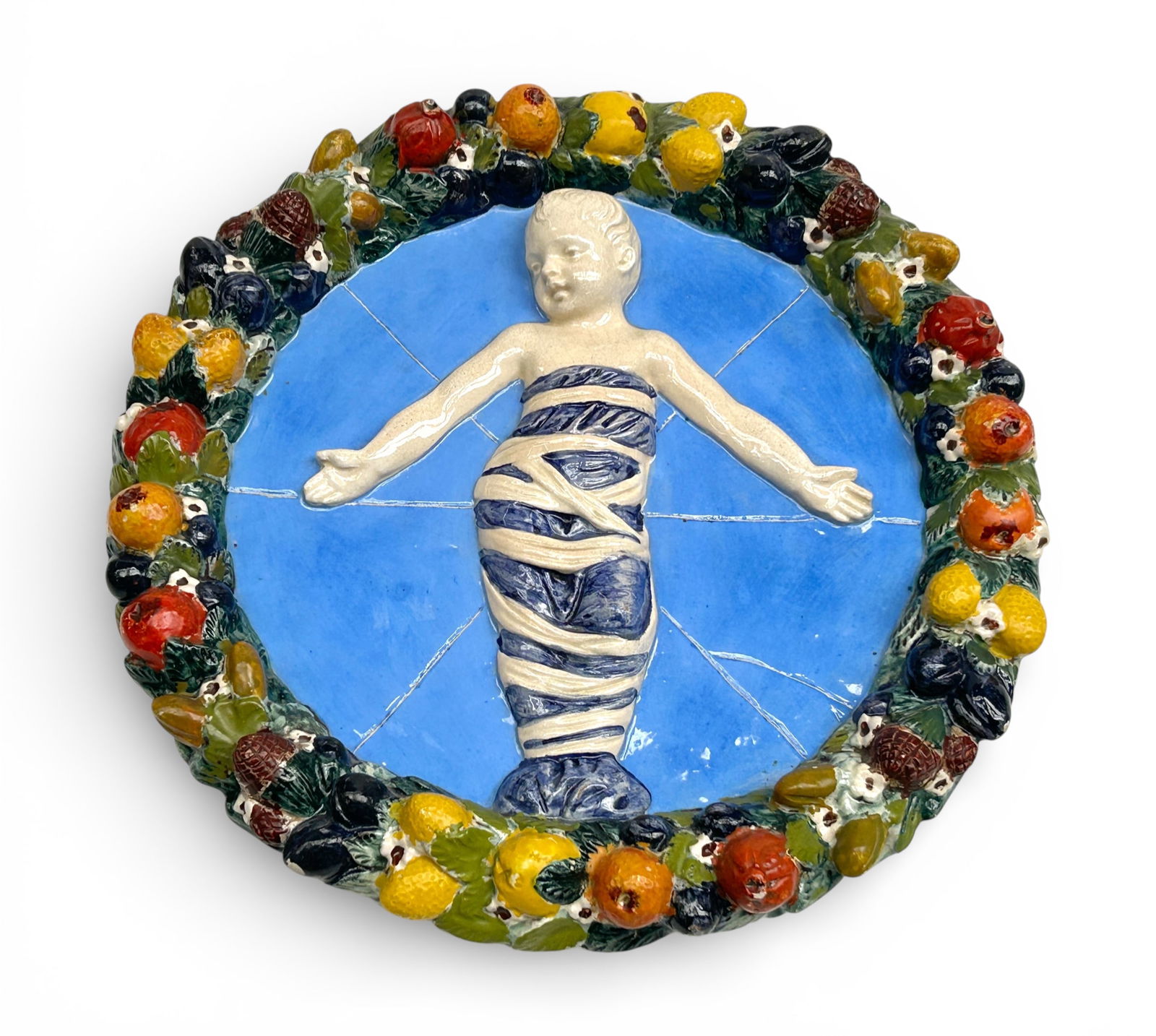 Della Robbia Tondo Plaque.: The item is marked Saca / 22d ? / Made in Italy on the back. It features a wrapped child in a Jesus-like position with a light blue background and a colorful fruit decorated rim. The piece is wired