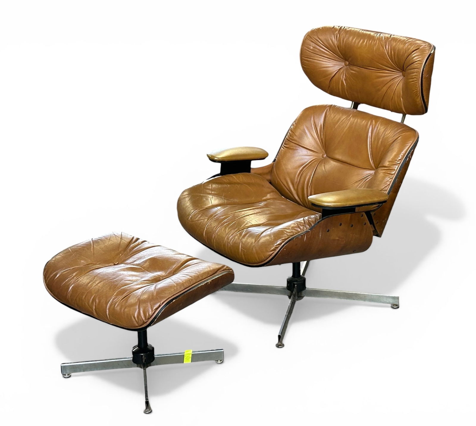 Brown Leather Eames Style Chair w/ Ottoman.: The bentwood chair and ottoman are upholstered with rich brown leather. They are unsigned. Both pieces have some damage to the veneer, and rust on the base/legs. The wood is sun faded. Overall, the