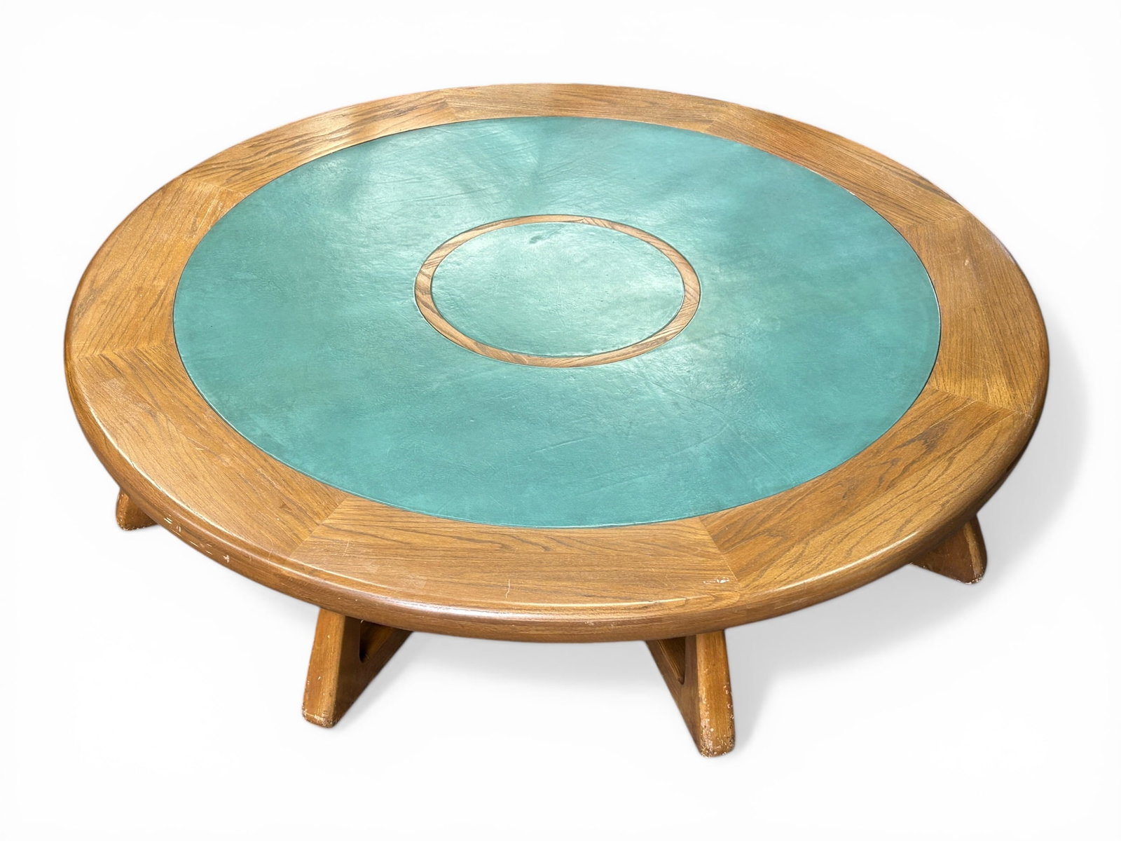 Large Low Leather Top Coffee Table w/ Horse.: This circular ranch style oak table has a green (faux?) leather top. It sits on eight legs that converge under the table. There is a carving of a horse where all the legs meet. There is some surface w