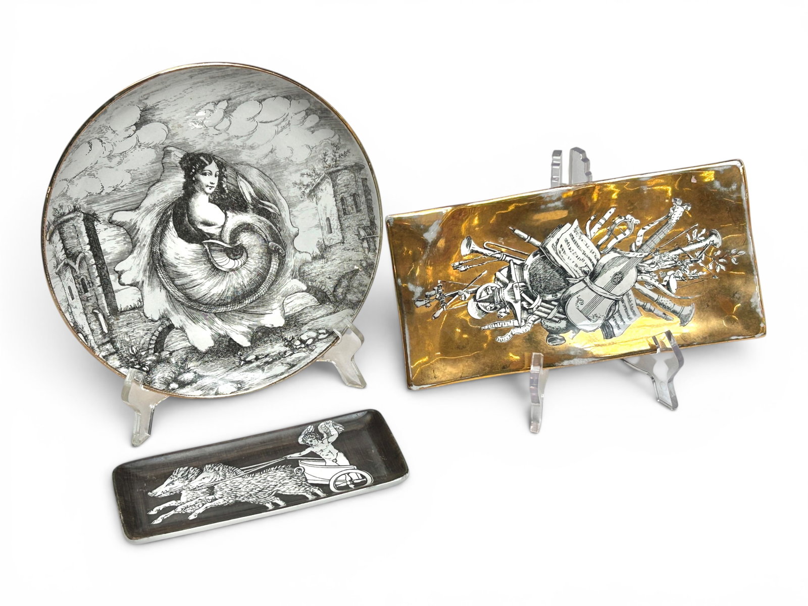 Lot of 3 Fornasetti Milano Italy Dishes.: The smallest plate bears an image of a cherub in a chariot pulled by giant boars. The next largest plate has a music motif. The largest plate shows a woman in a large seashell. All three look to be in