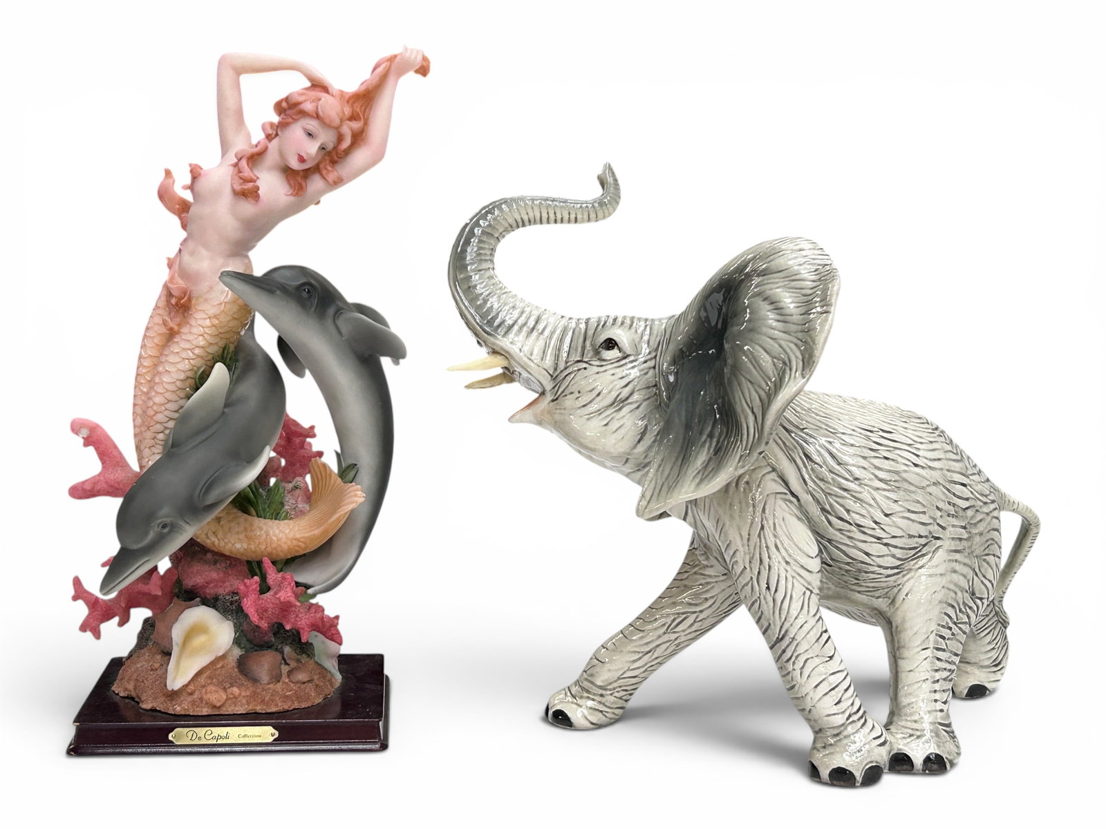 2 Sculptures - Elephant & Mermaid.: The lot contains 2 sculptures. There is a high glaze porcelain elephant with a Made in Mexico sticker, and a composition piece depicting a mermaid among dolphins and coral by De Capoli Collection. The