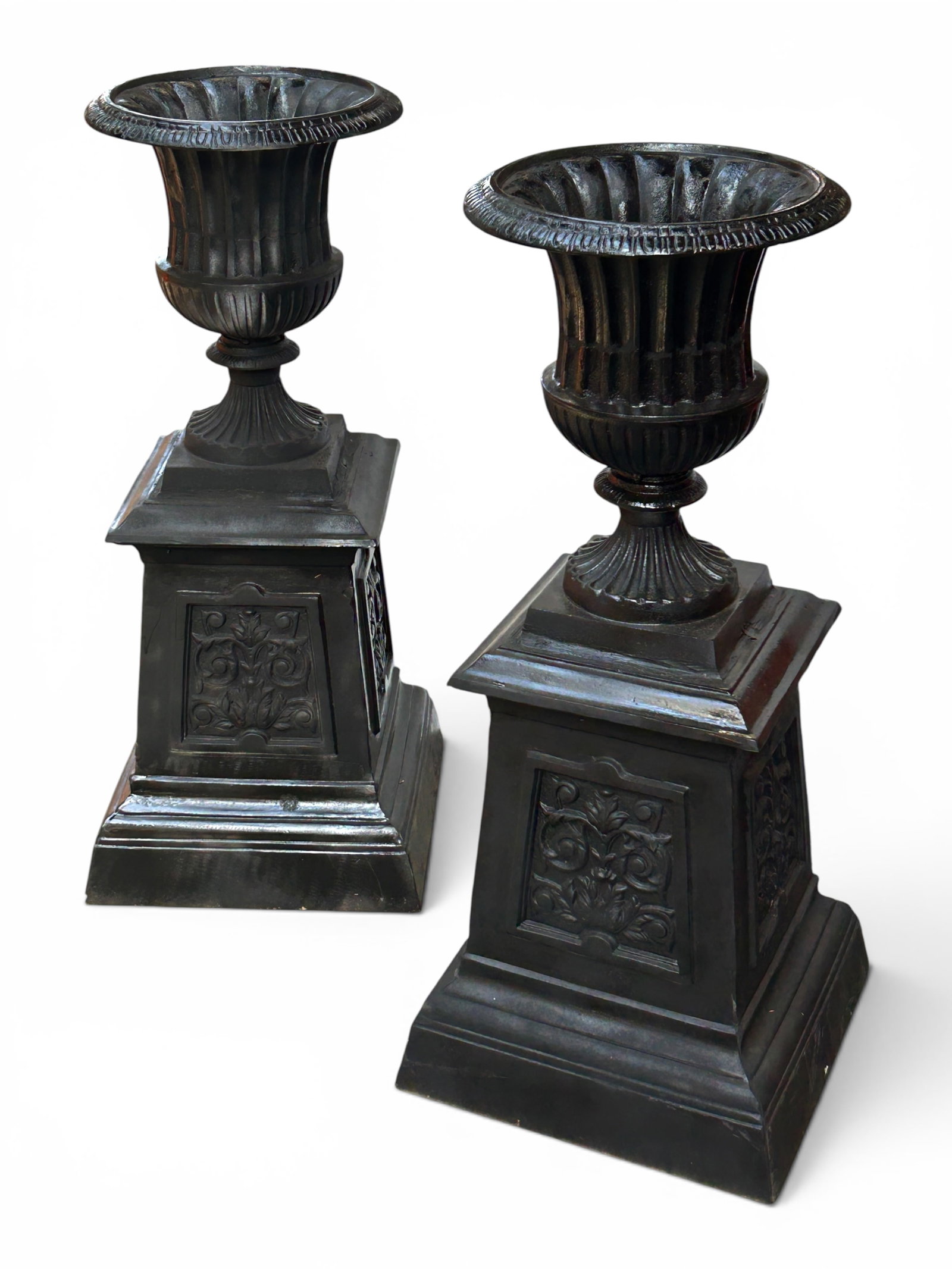 Pair of Tall Metal Garden Urns.: The urns are made of aluminum, and meant to resemble cast iron. They depict sculpted vases on stands, with floral decorations on the sides. They are stamped "Made in Mexico" on the bases. There are a