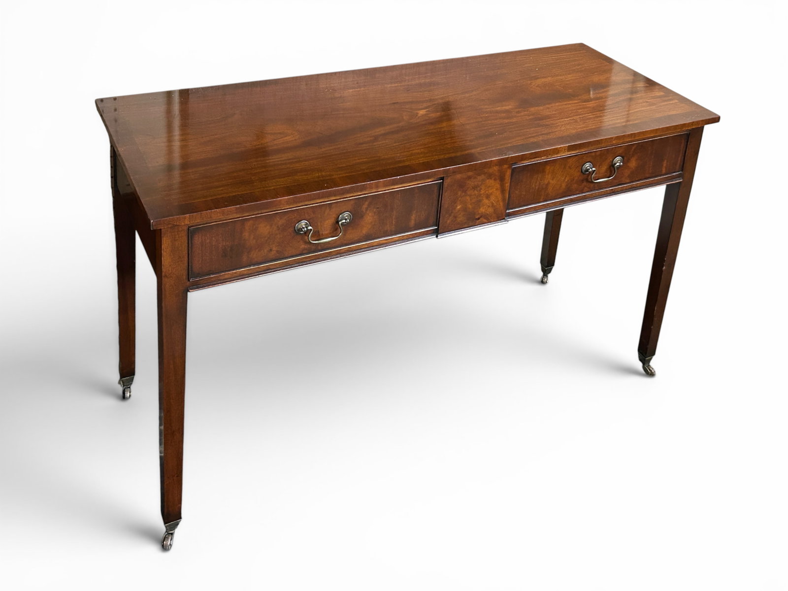 George III Style Flame Mahogany Desk on Casters.: The two drawer desk has brass drawer pulls and casters on the slightly tapered rectangular legs. It measures 29 1/4" tall, 48 1/4" wide, and 19 1/8" deep. About 1 1/4" of trim from under one of the dr