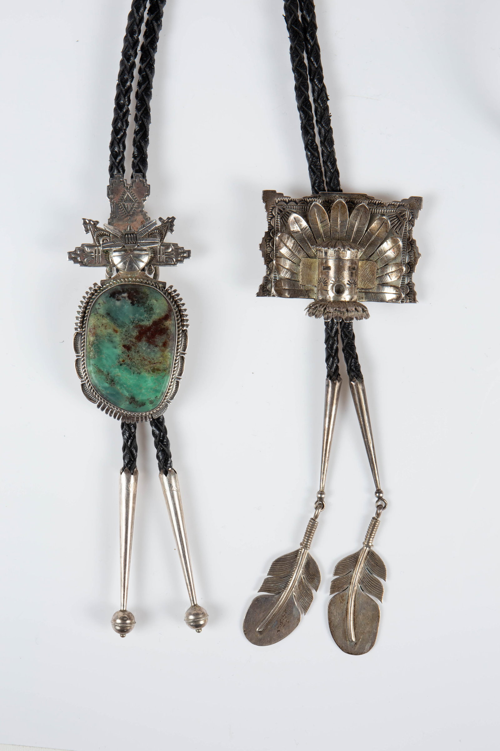 2 Kachina Bolo Ties by Benny Ration.: The lot contains 2 sterling silver bolo ties by Native American Navajo Indian artist Bennie Ration. Both slides feature sculptural Kachina doll representations, and one of them also has a large stone.