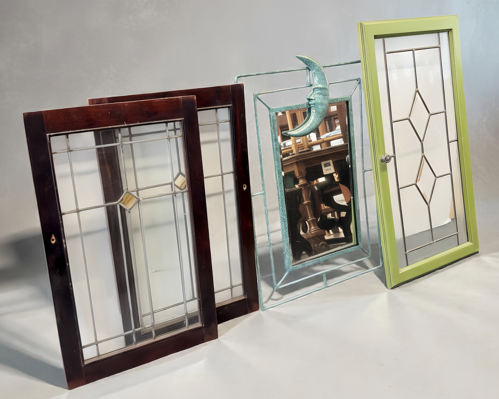 Lot: Iron Mirror & 3 Leaded Windows, inc. Prairie.: The lot contains 4 items. There is a beveled mirror with an iron frame and a moon face figure and a green patina finish, 2 prairie style stained glass windows, and a leaded etched glass cabinet door. 