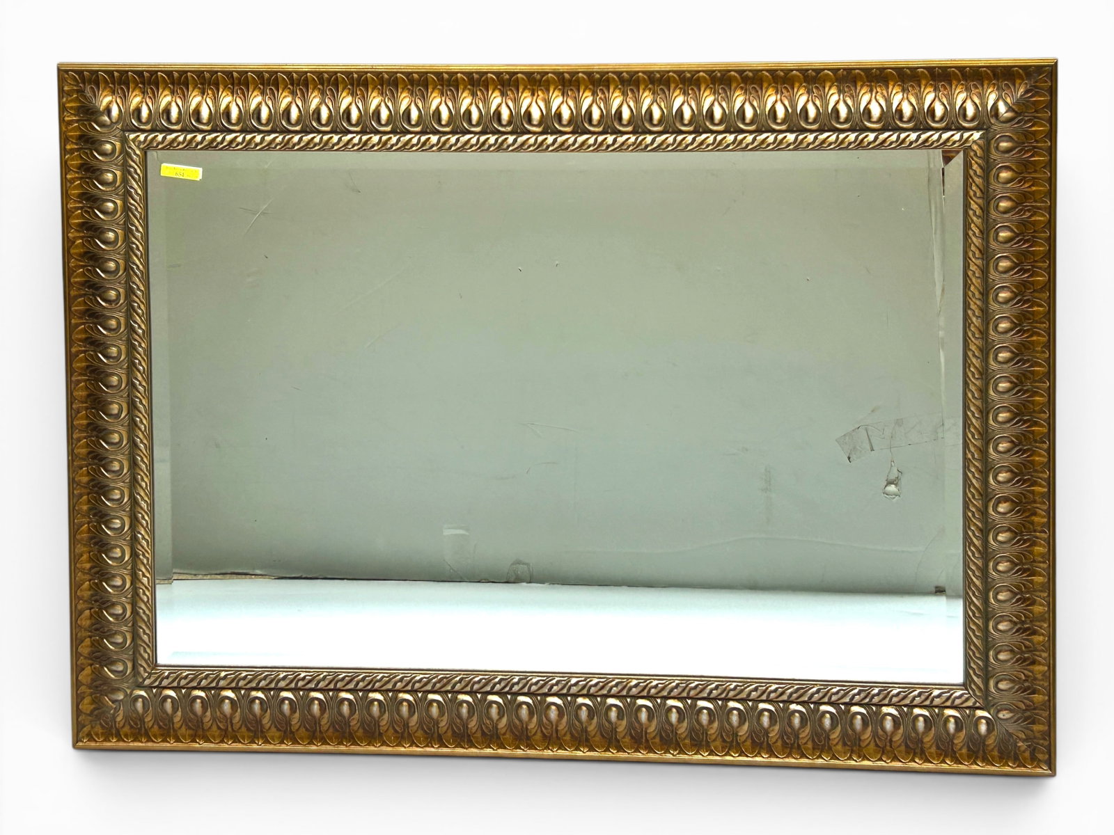 Ornate Neoclassical Style Gilded & Bevelled Mirror: The mirror features a tongue or egg and dart gilded relief pattern on the 3 7/8" wide frame. The piece measures 31 3/8" x 43 1/8". It is fitted with a wire to be hung horizontally. There are minimal s