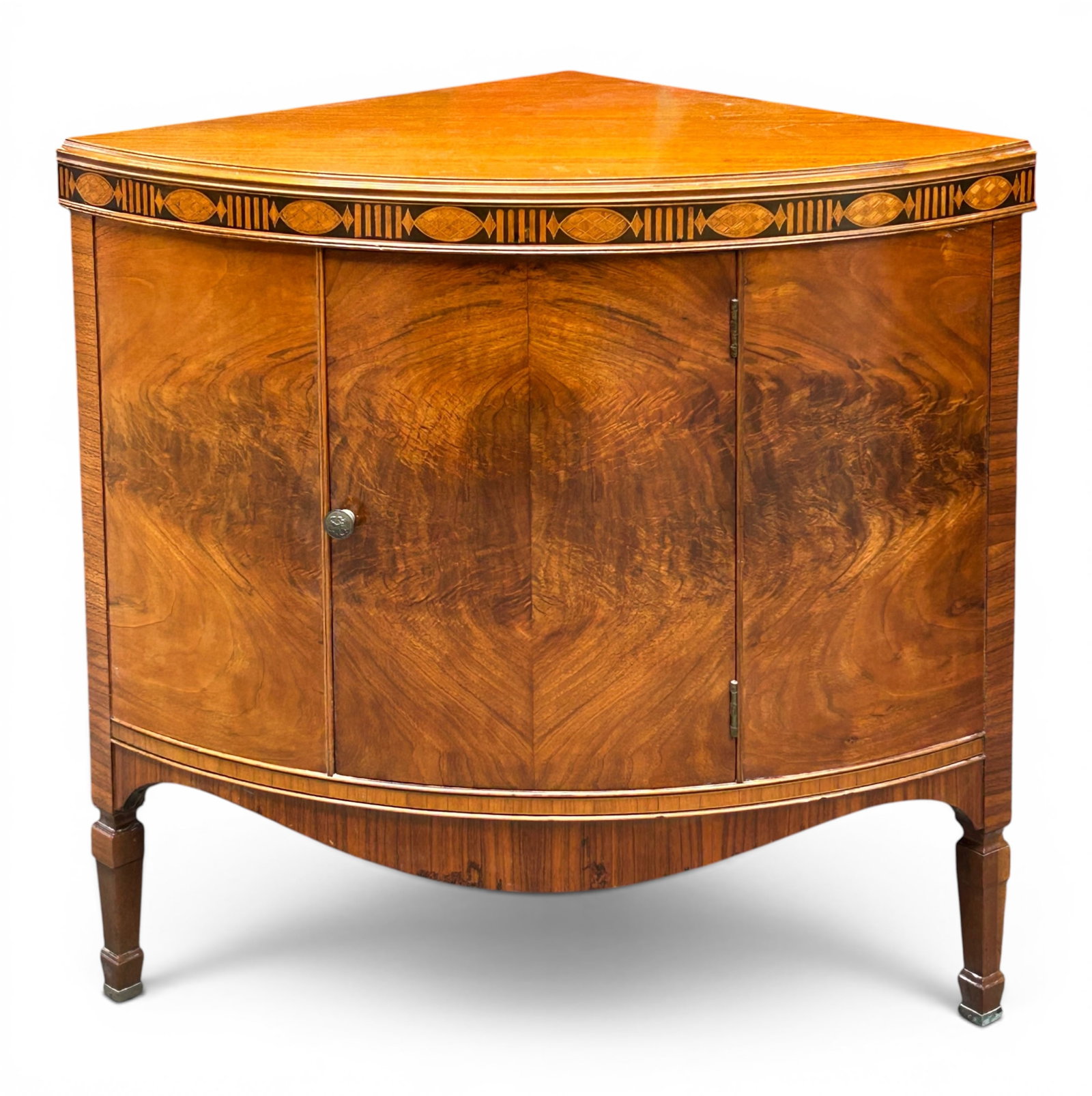 Flame Mahogany & Inlaid Small Corner Cabinet: The federal style cabinet table has a rounded front with flame wood veneer, and and an inlaid wood pattern on the top edge. The piece has one shelf inside, and tapered legs with brass lined feet. It m