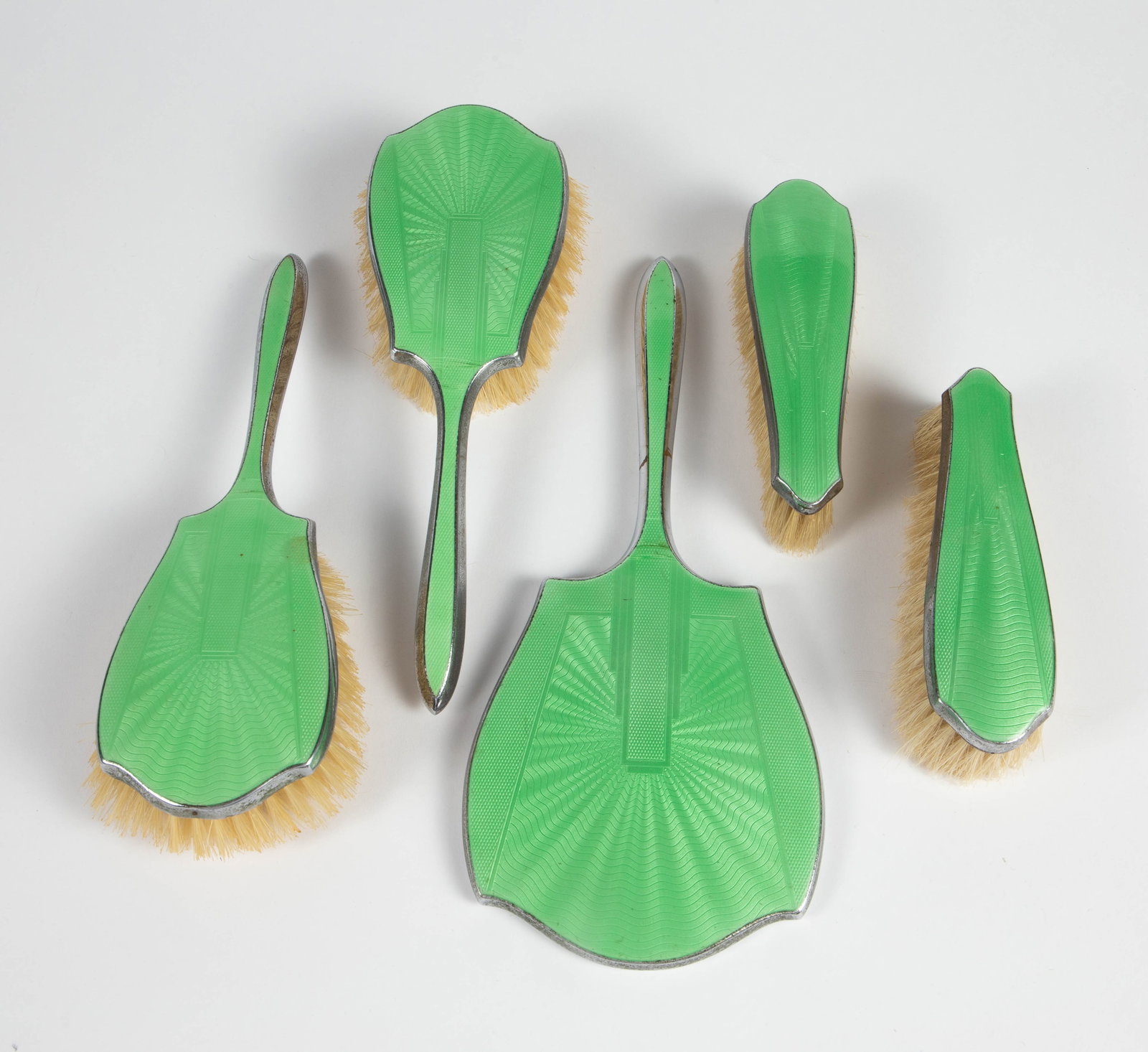 5 Pc. Green Guilloche Enamel Vanity Brush Set.: This silverplate set looks to be in overall good condition, with some signs of use. Two of the brushes are marked as English. There are four brushes in total, and one hand mirror. The largest item in