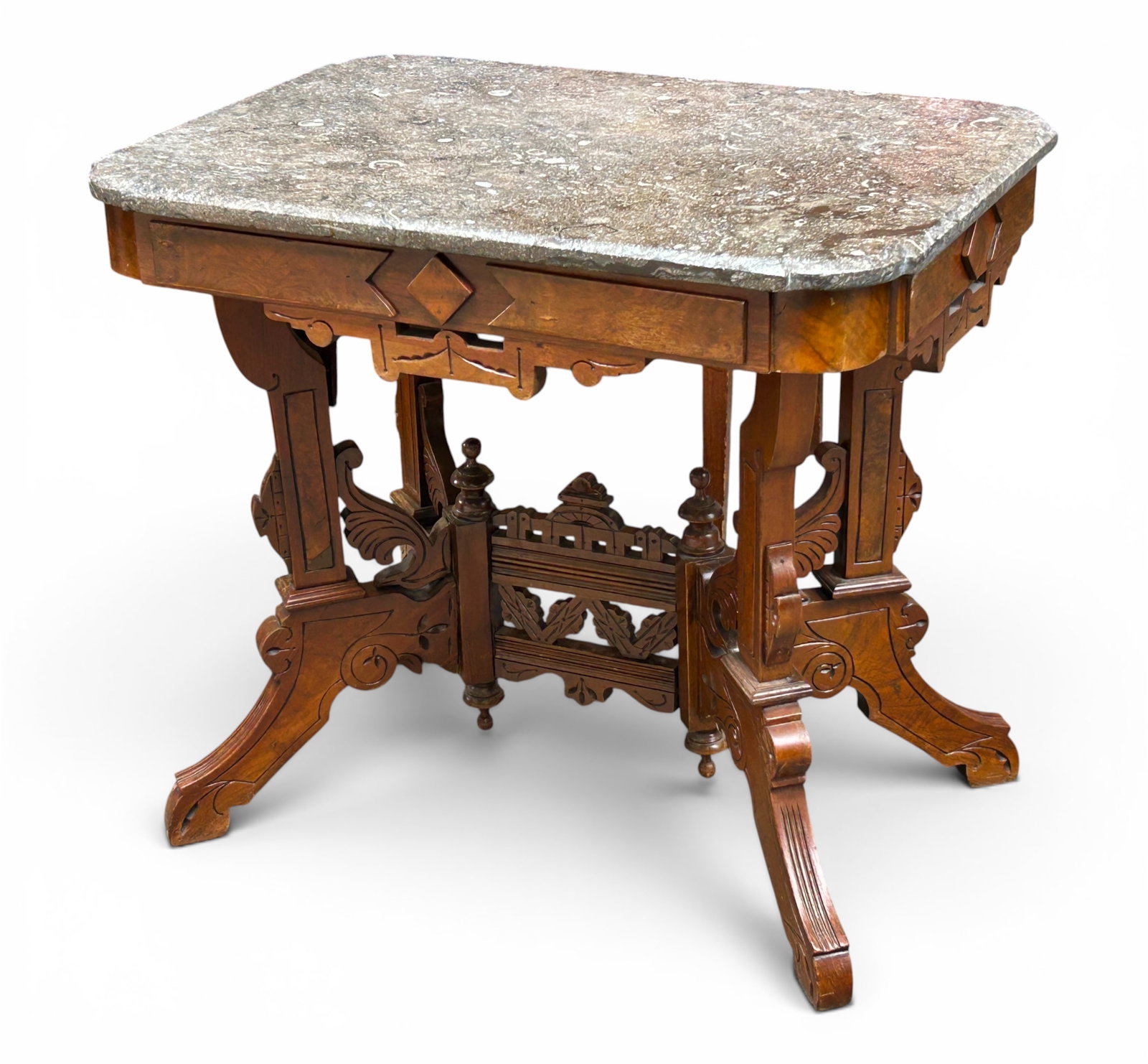 Victorian Eastlake Marble Top Table.: This parlor table has a burled wood base, carved details, turned finials, and a trestle base. The apron has multiple carvings. The marble top has some dark spots and minor chips on the sides. There ar