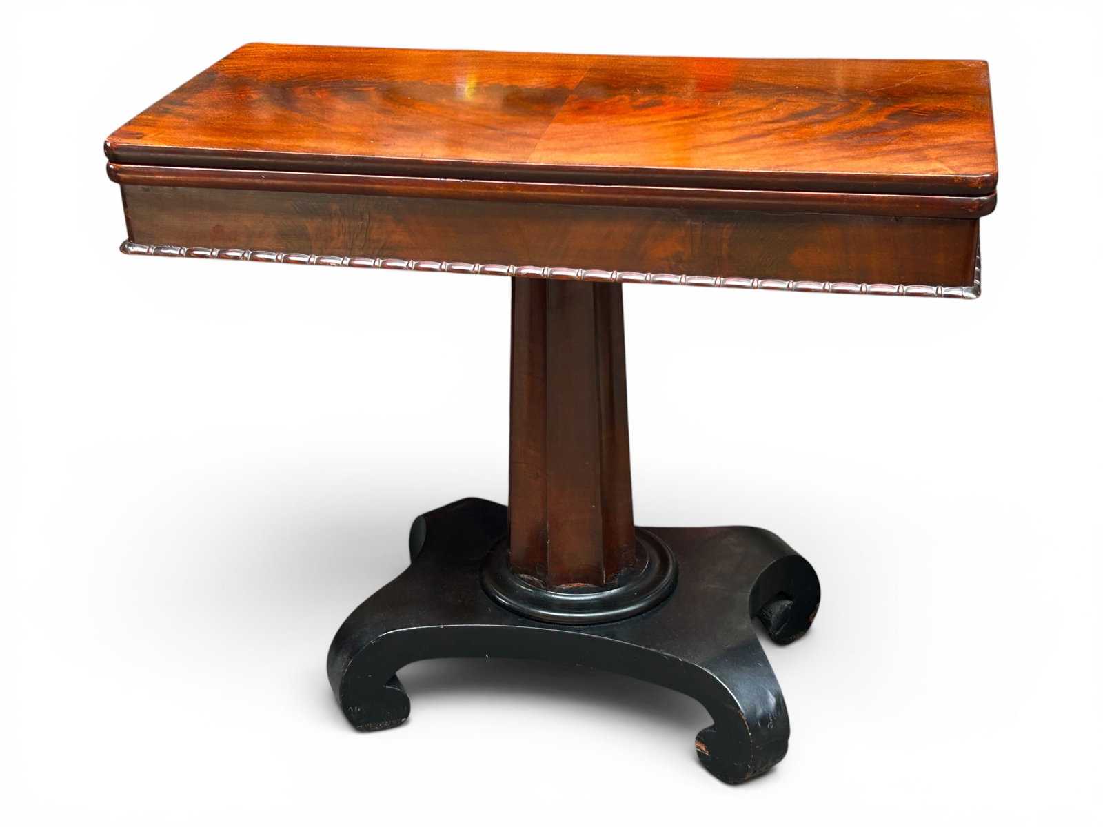 Empire Flame Mahogany Game Table.: This game or card table has a rotating flip top that opens up, pedestal legs, and an ebonized base. The apron is carved. There are some scratches on the unopened top. Overall, it is sturdy and