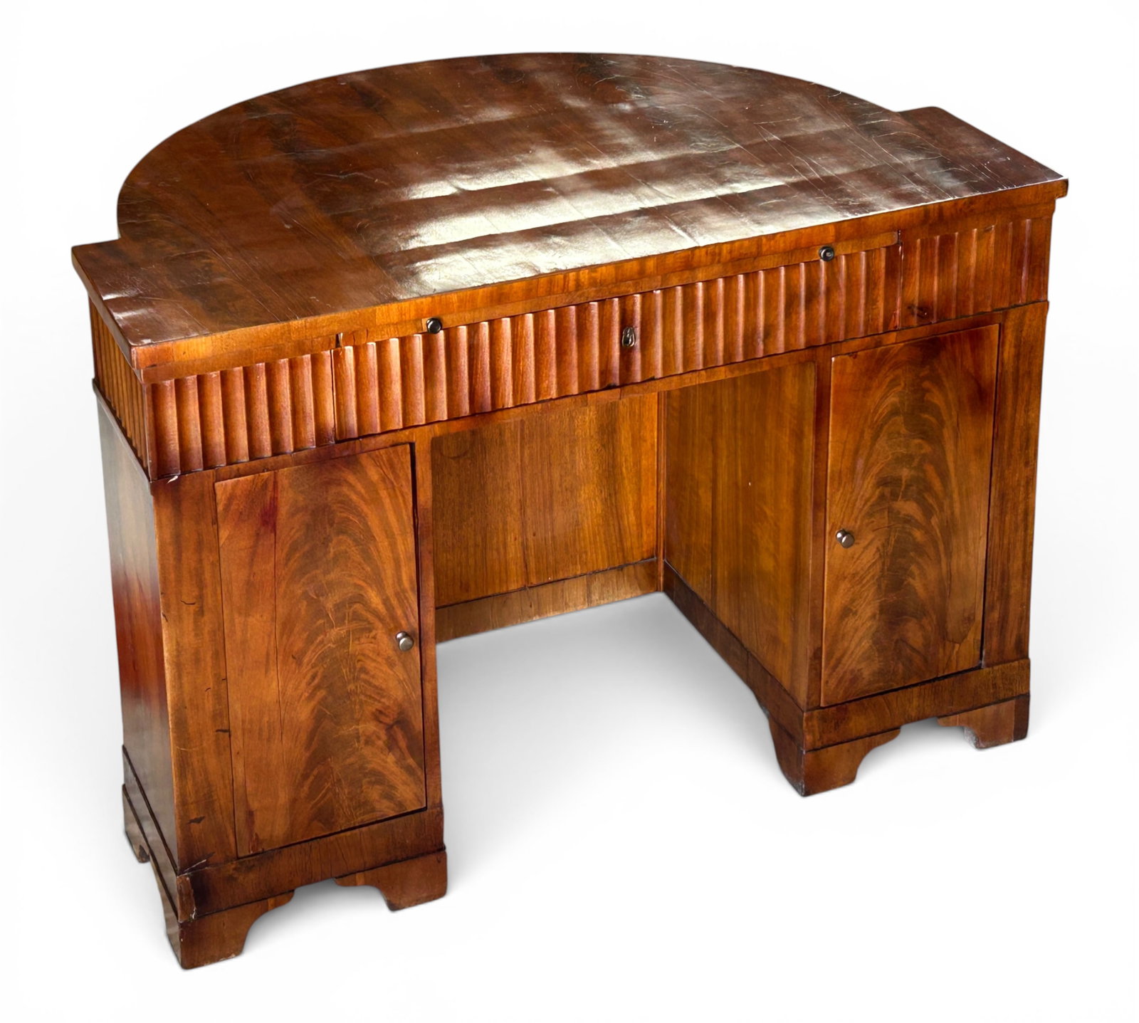 Flame Mahogany French Art Deco Desk.: This desk has a semi-circular design, a pull-out writing tray with a leather insert, two front doors with removable shelves, and a rear door with an interior storage compartment. Overall, it is in