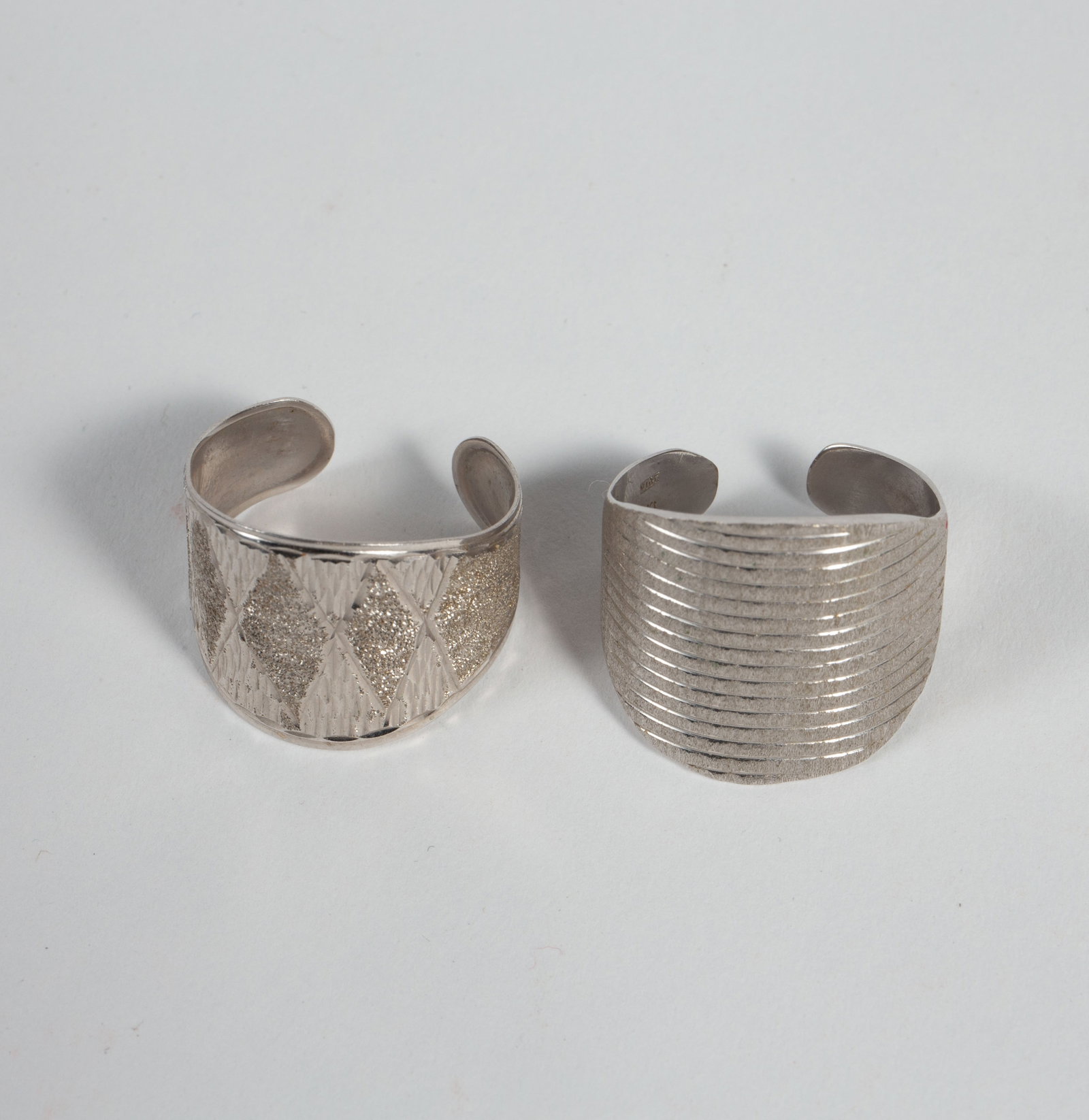 Two 14K White Gold Rings - Vior Italy, SLC.: The lot contains two adjustable or open rings with wide surfaces. The ring with a ribbed linear design is marked Vior 14K Italy, and the piece with an etched harlequin diamond design is marked SLC 14K