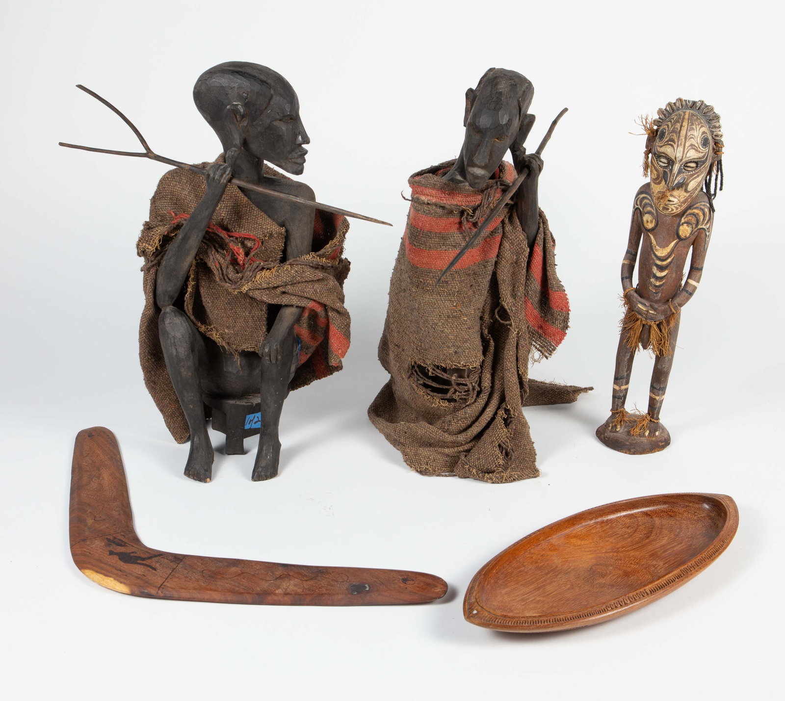 Ethnographic Carved Wood Items, Figures, Boomerang: The lot contains 5 items. There are two African seated male figures wearing woven cloths with spears on their hands. The next two items are likely from Papua New Guinea. There is a carved elongated