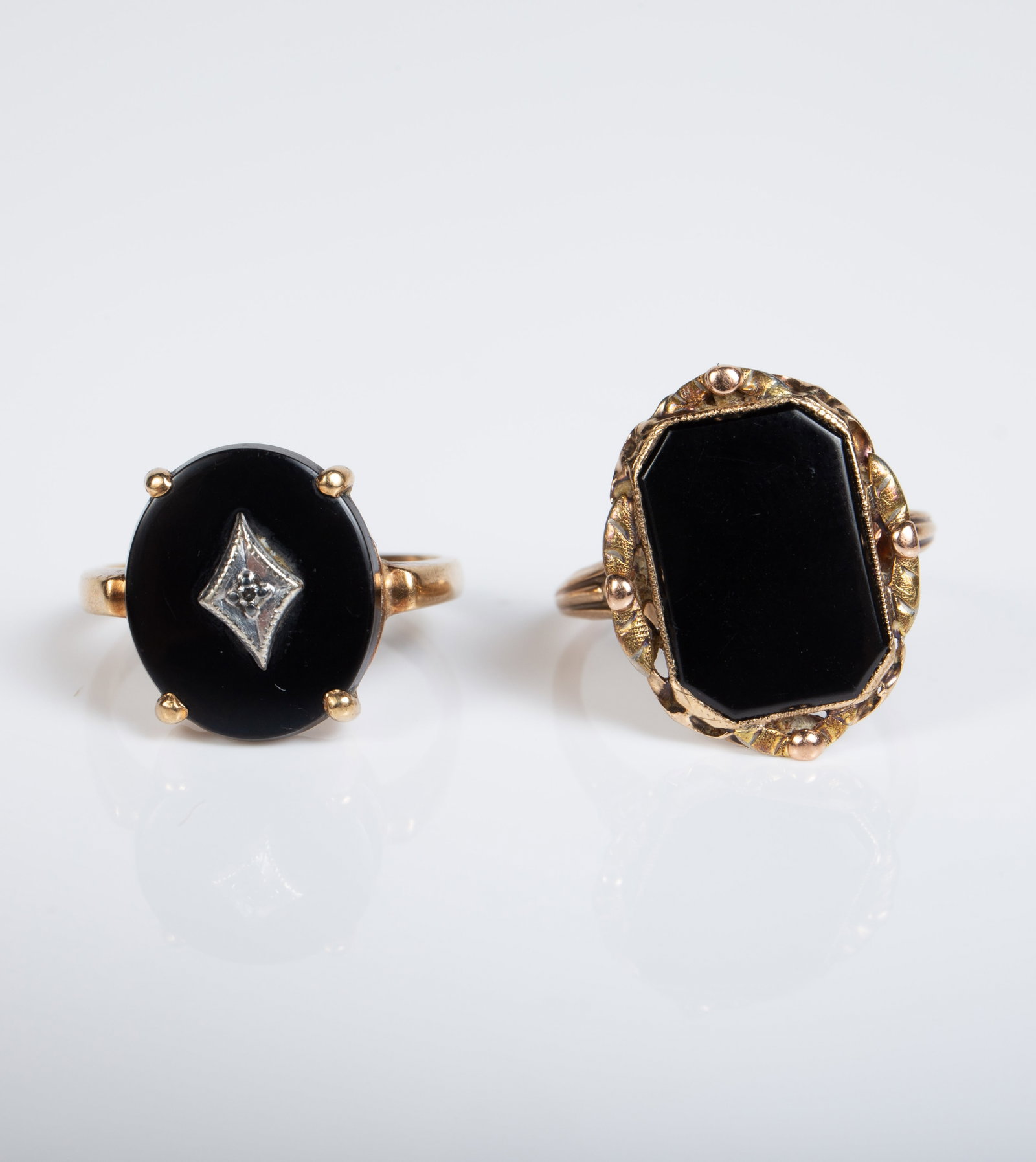 Two Vintage 10K Gold & Onyx Rings, inc. Diamond.: The lot contains 2 antique-style yellow gold rings with large black onyx surfaces. The first piece is by Budlong, Docherty & Armstrong, and has an octagonal stone with an ornate border. It is marked B