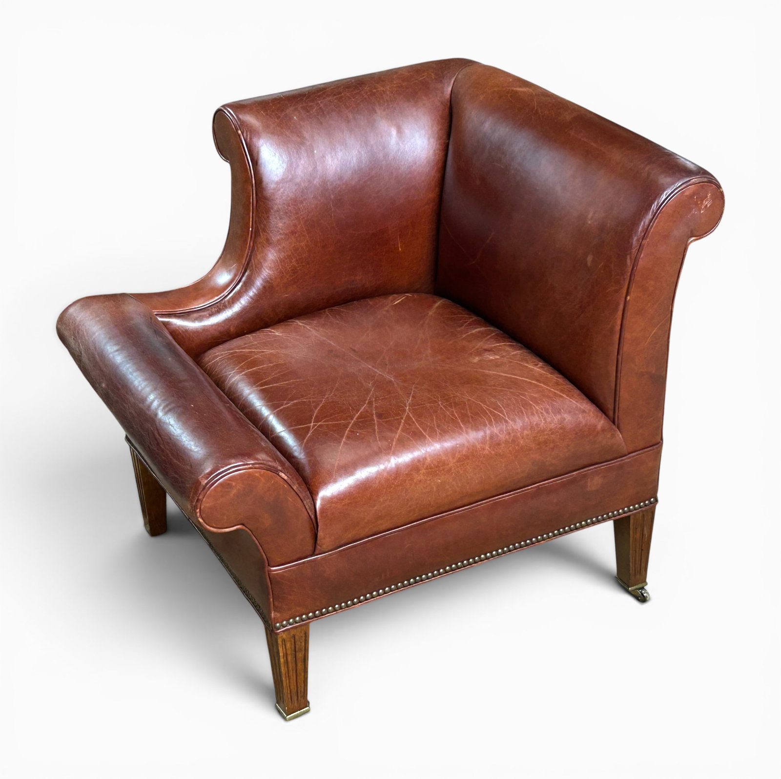 Unusual Brown Leather Club Corner Chair.: The vintage leather chair has tapered legs with vertical linear carvings on brass casters, brown leather, and brass nail head trim on the bottom edge. It has two backrests that meet at a corner, and