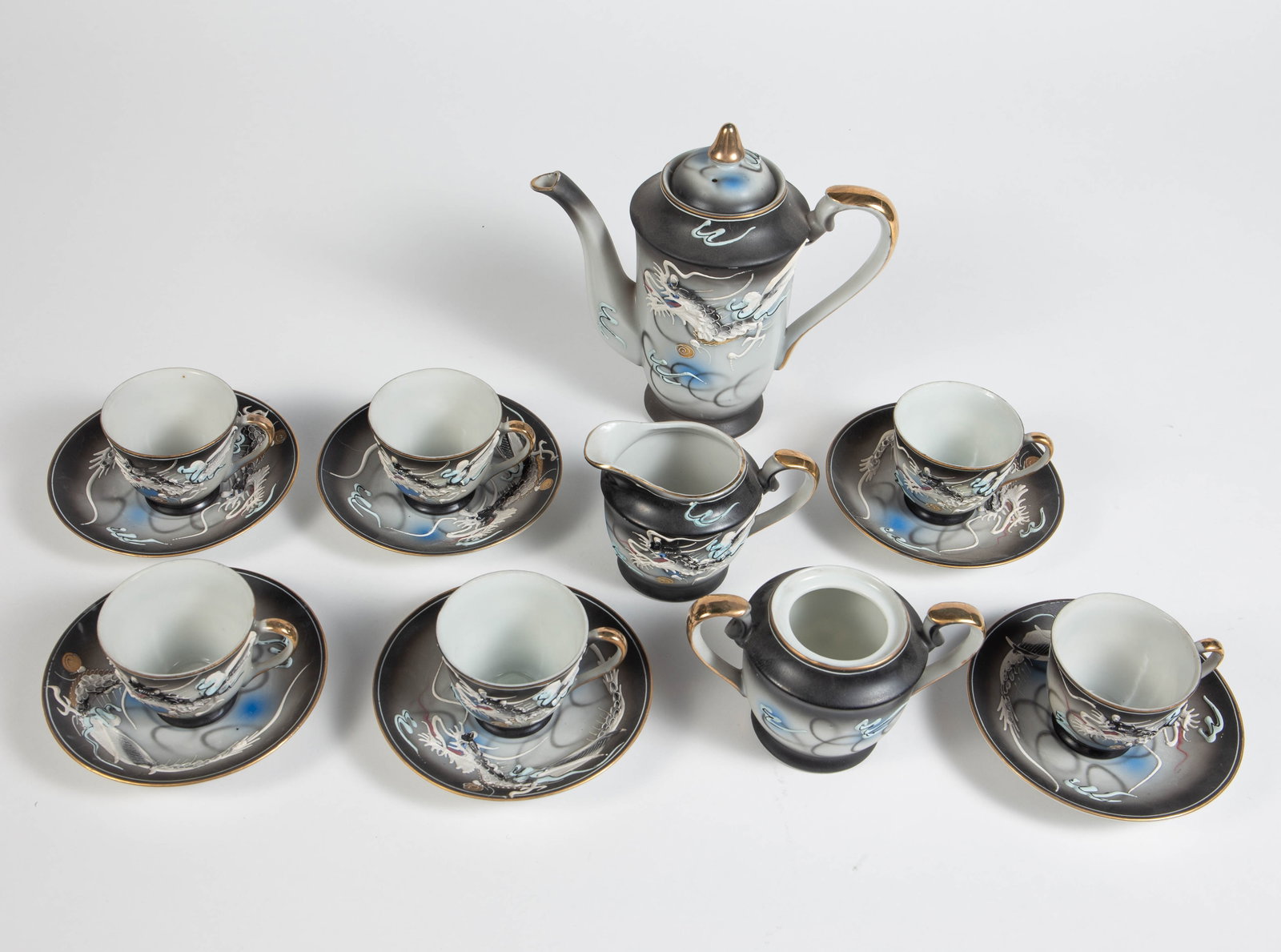 Vintage Moriage Lithophane Japan Dragon Tea Set.: This set includes six demitasse cups with matching saucers, a sugar bowl, a creamer jug, and a small teapot with lid. The cups have lithophane bottoms, with an image of a geisha girl's head seen at th