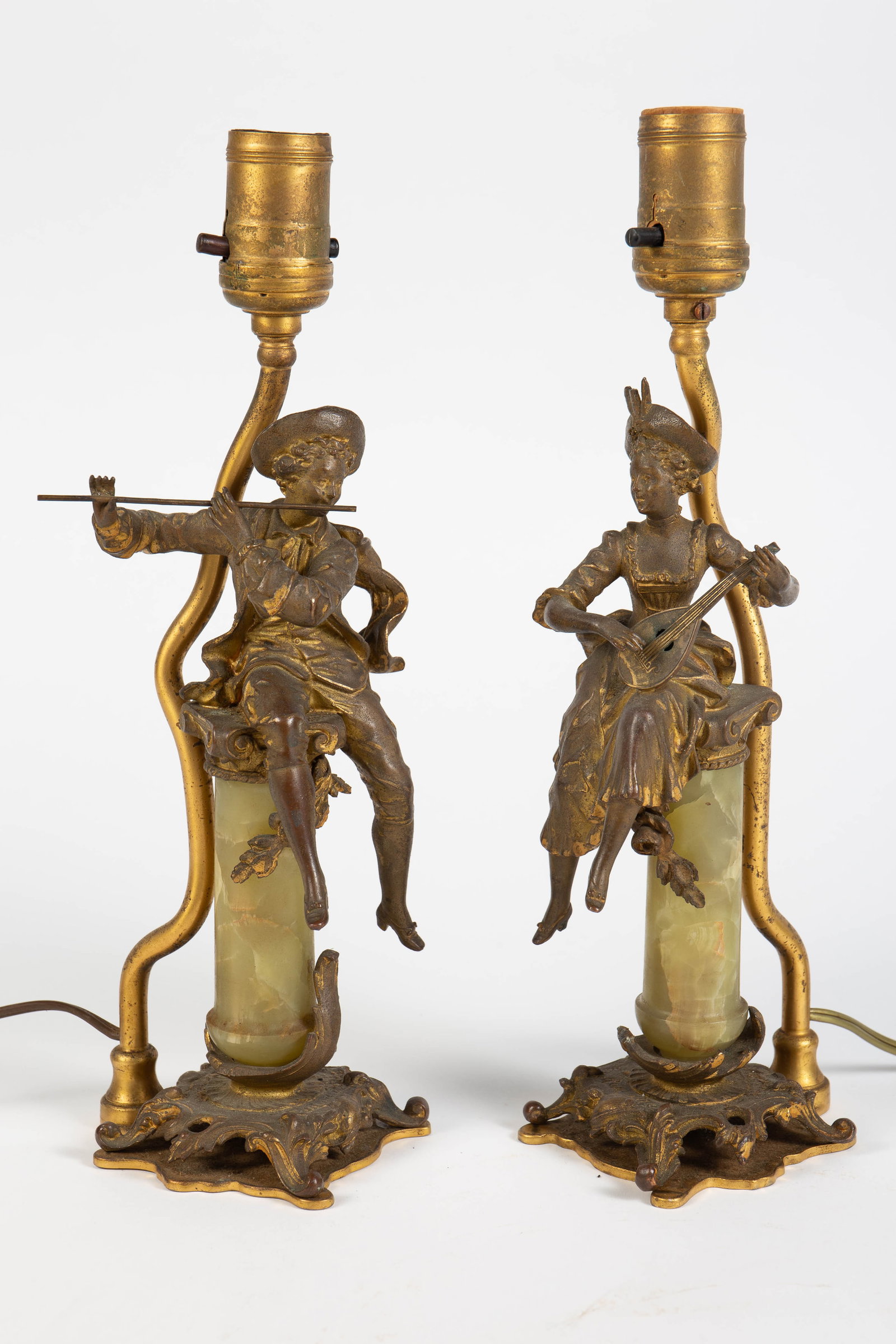 Pair of Musician Lamps Signed "Rancoulet".: One is a male flute player, the other is a female mandolin player. They are most likely gilded spelter. The pillars they are sitting on appear to be onyx. Both lamps display signs of surface wear,
