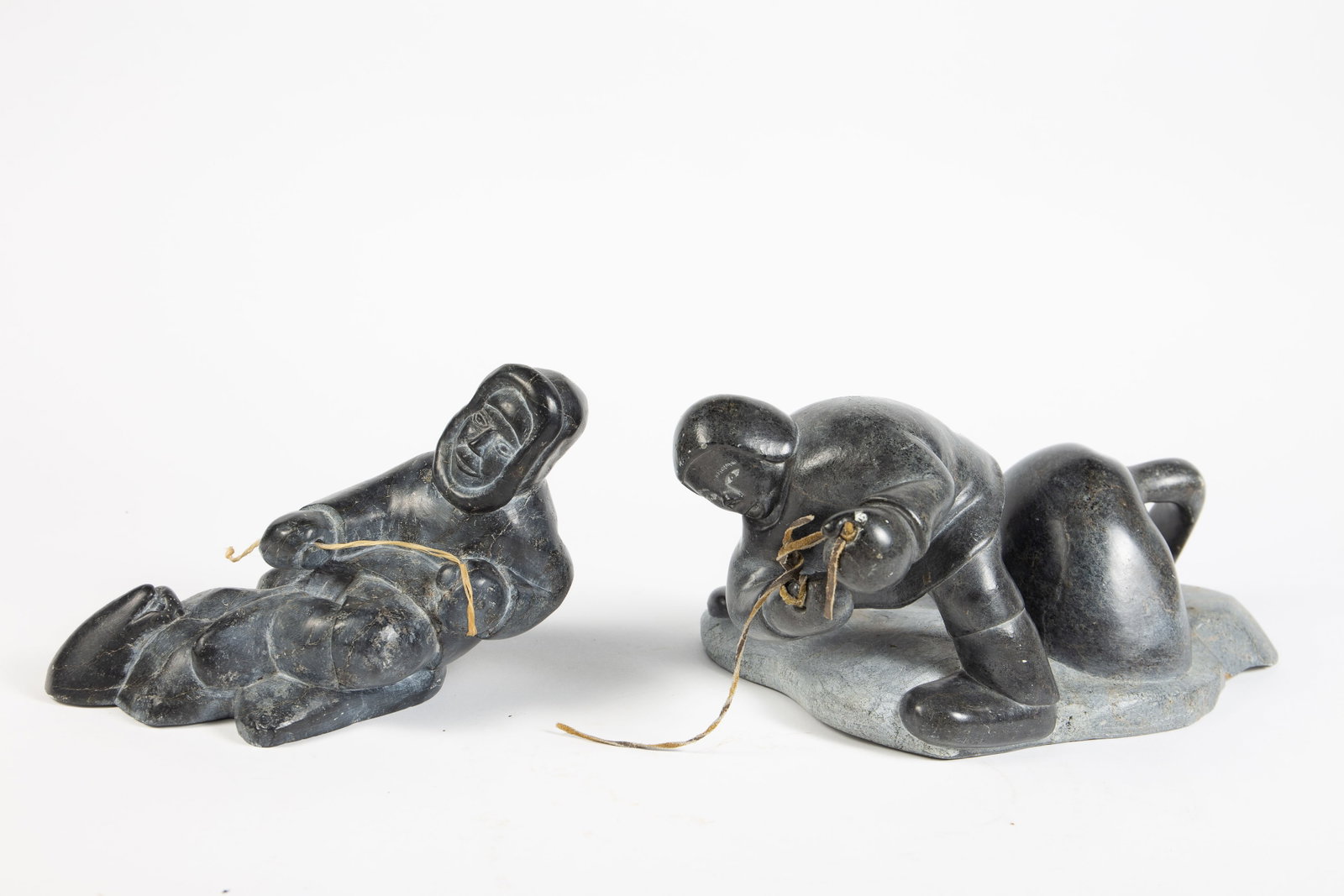 Lot of 2 Carved Inuit Sculptures, inc. Qumaluk.: Both sculptures depict seal hunters. The larger one has a label attached underneath, identifying the artist as Qumaluk. It measures 13" x 7 7/8" x 5 1/4". The other sculpture is by an unknown artist,