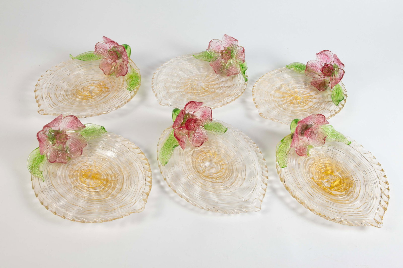 Set of 6 Pink & Green Venetian Glass Flower Plates: They have a gold shimmer, and are shaped like leaves. They appear to be unsigned. Overall, they look to be in nice condition. Each plate measures approximately 9 3/8" x 7 1/8" x 3 3/8". In-house