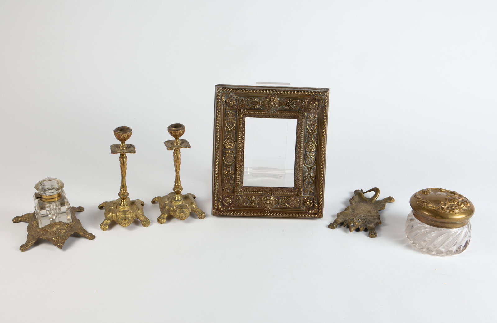 Lot of Brass or Bronze Desk Items w/ Lion Motif.: The brass-clad wood frame has North Wind and lion faces. The inkwell holder, pen rest, and candlestick pair all resemble lion rugs. The Art Nouveau style vanity jar is the only item with a flower moti