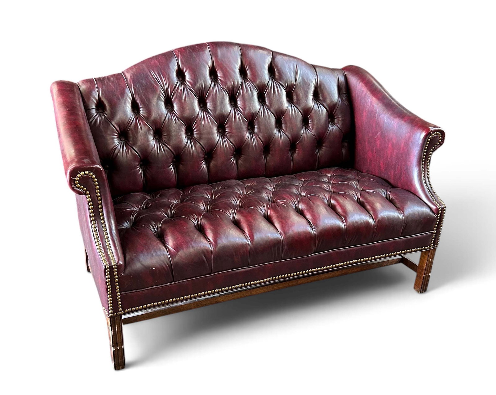 Red Chesterfield Loveseat - Faux Leather.: This Chippendale style chesterfield loveseat features a faux leather button tufted design, brass nailhead trim, and a camelback shape. The faux leather is in good condition, with some wear marks. One