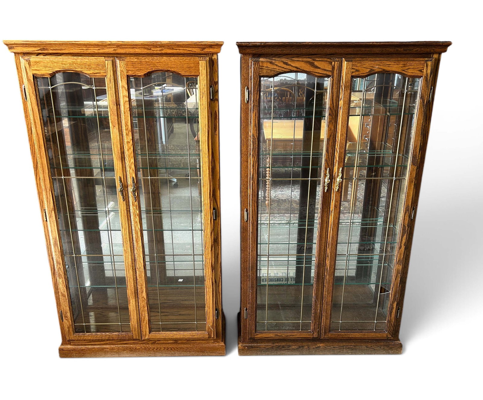 Pr. Illuminated Oak Curio Cabinets or Bookcases.: The lot consists of 2 cabinets in different tones of wood. They have leaded glass doors, four adjustable glass shelves, and mirrored backs. They measure 60 1/2" tall, 35" wide, and 14" deep. One of