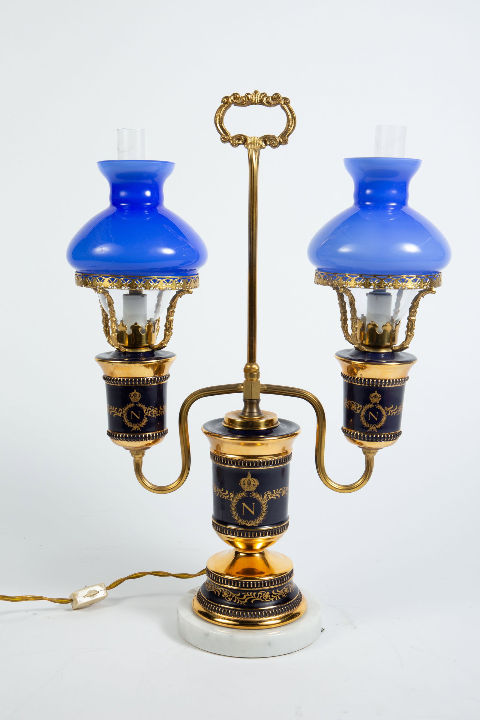 French Lamp w/ Napoleonic Motif, Cristal De Roche.: The two-arm carriage table lamp has a marble base and a gilded body with black banded sections and Napoleonic designs. It has blue decorative crystal chimney shades, with interior clear chimney shades