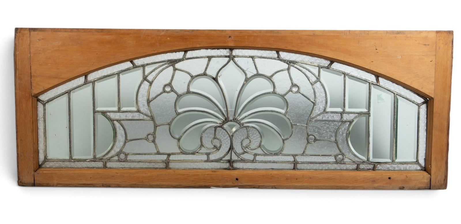 Antique Arched Beveled Leaded Glass Window.: The window features beveled and textured glass with a few multifaceted jewel accents. It has a central scrolled fan design. The wooden frame measures 17 3/4" x 48". The piece is dented on one corner, 