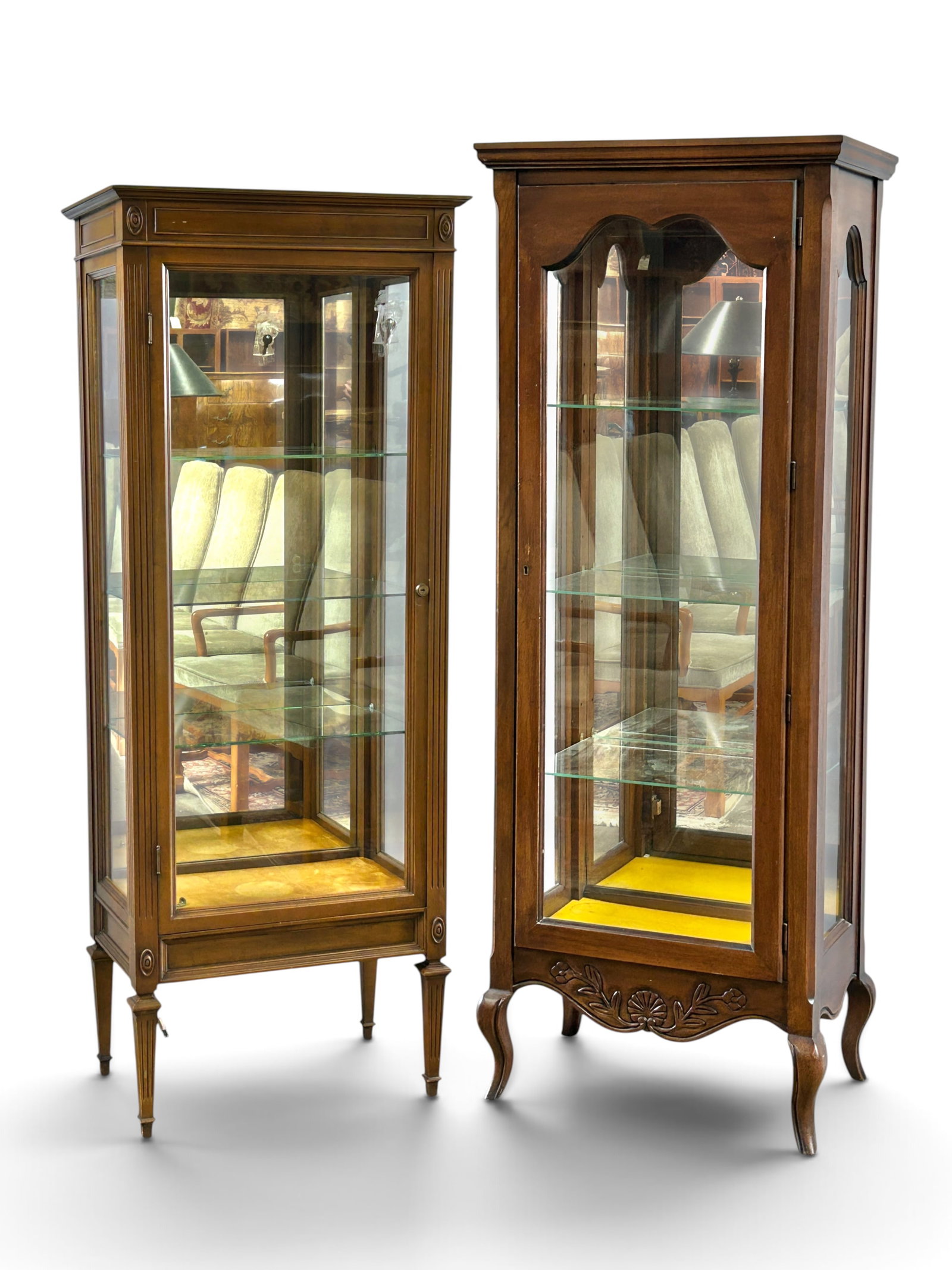 2 Illuminated Carved Curio Display Cabinets.: One of the cabinets is signed Hekman. The lot consists of 2 tall distinct curio cabinets, each with 3 glass sides, a mirrored back, one front door, and 3 interior glass shelves. Only the shorter piece