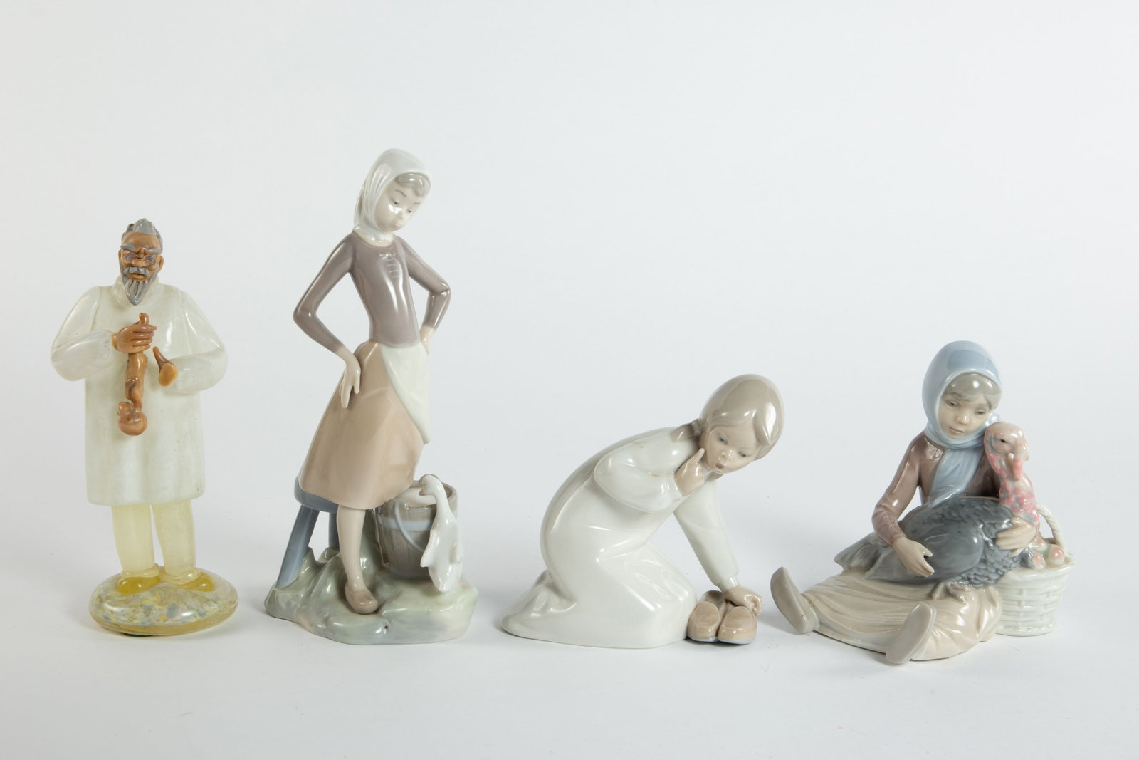 Lot: 4 Pcs.- Lladro Figures, Bohemian Glass Doctor: The Lladro figurines are young girls (the girl with the turkey has had her foot repaired). The largest of these measures 4 1/2" x 3 1/2" x 9 3/4". The Bohemian glass doctor is holding a newly